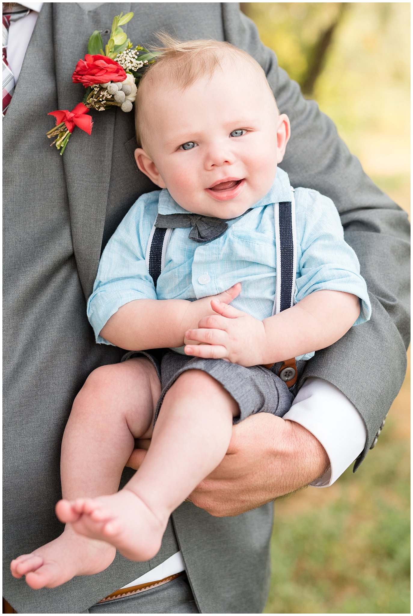 Smiling baby ring bearer in bow tie and suspenders being held by the groom | Davis County Outdoor Wedding | Jessie and Dallin Photography
