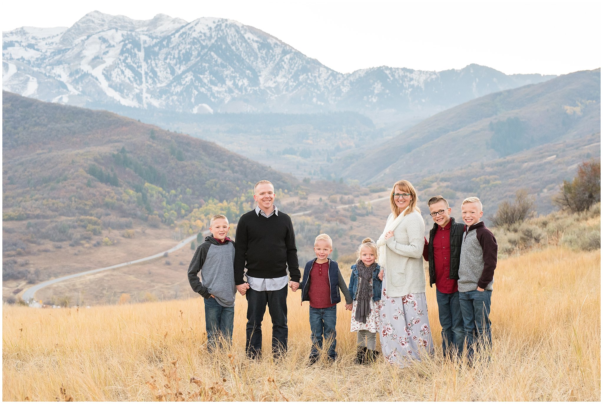 Family with five kids holding hands in front of snowy mountains | Fall Family Pictures in the Mountains | Snowbasin, Utah | Jessie and Dallin Photography