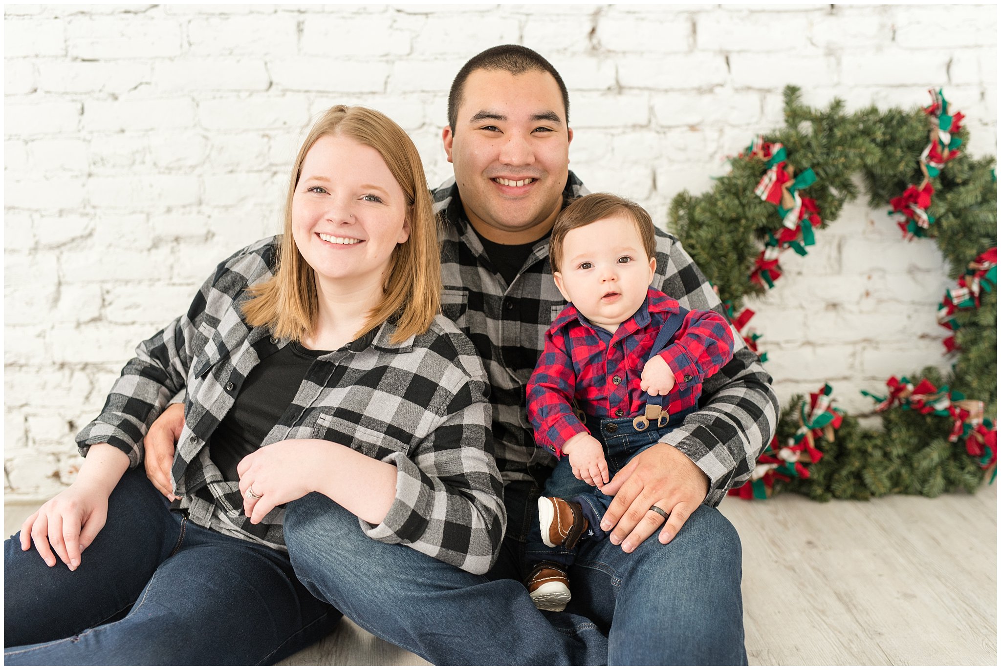 Family smiling at the camera with Christmas wreath behind them | Family Christmas session at the 5th floor | Utah Photographers | Jessie and Dallin Photography