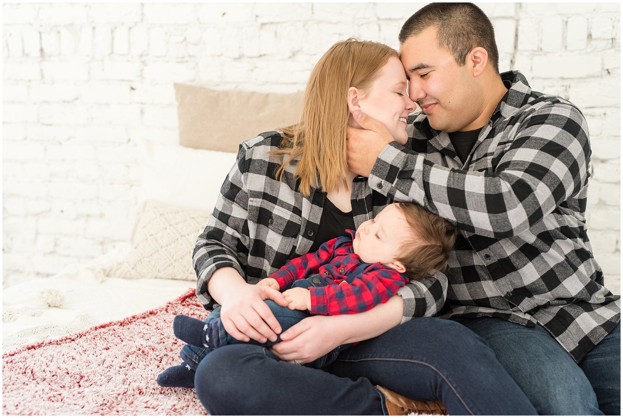 Parents nuzzle close and hold sleeping baby boy on bed | Family Christmas session at the 5th floor | Utah Photographers | Jessie and Dallin Photography