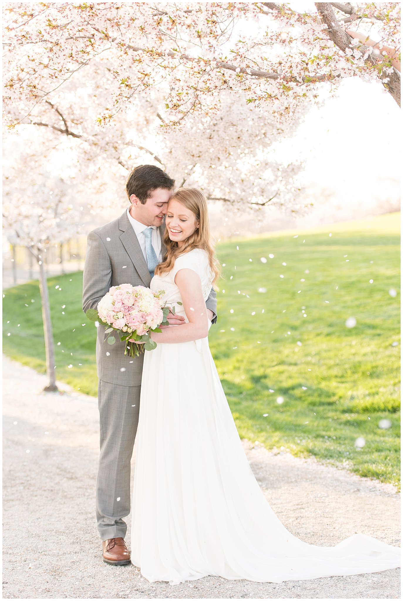 Bride with blush bouquet and groom with grey suit in the cherry blossoms with falling petals | Utah State Capitol Blossoms Formal Session | Salt Lake Wedding Photographers | Jessie and Dallin Photography