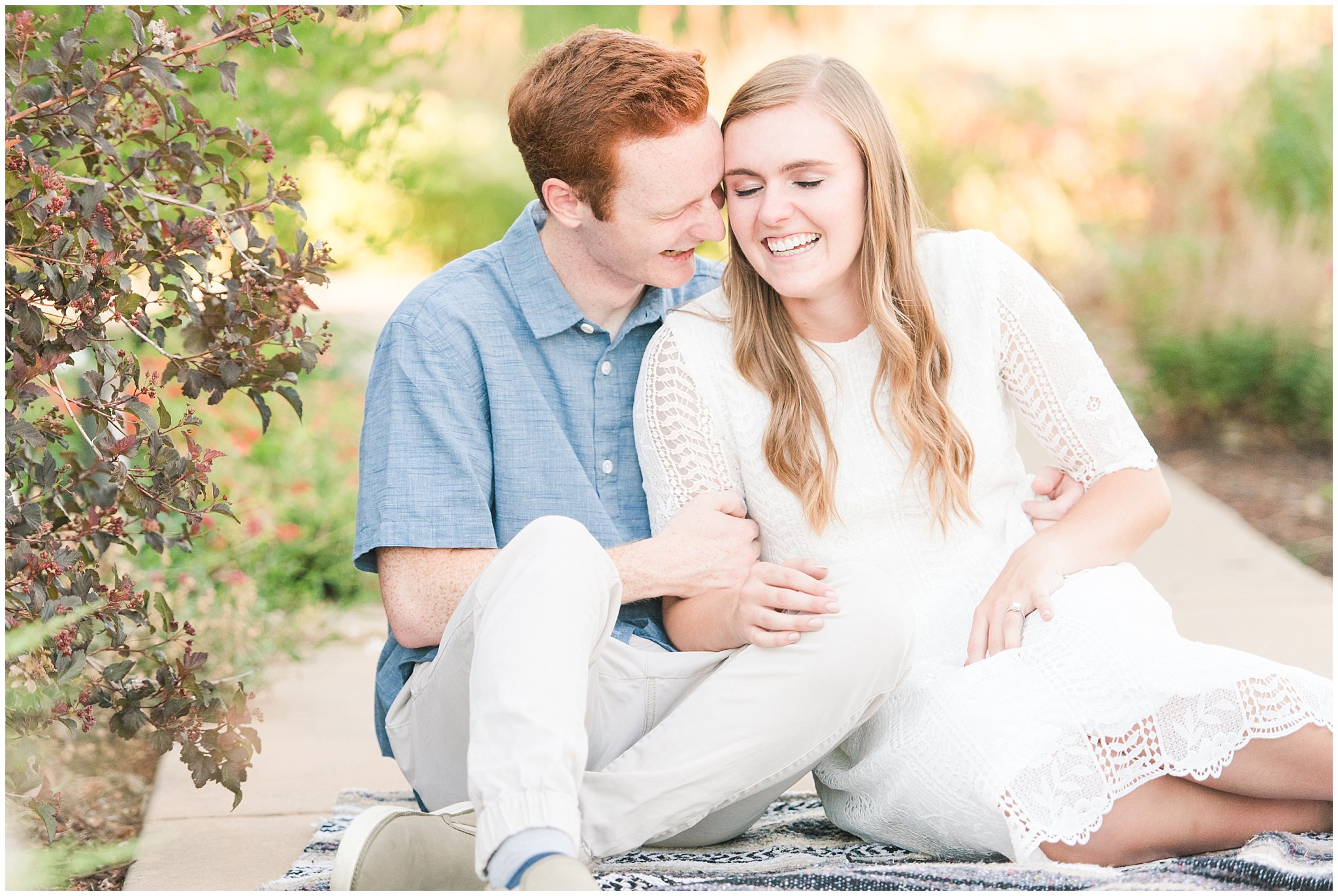Couple wearing a white lace dress and light blue shirt during candid engagement photos in a Utah garden with flowers and a pond | Kaysville Botanical Garden Engagement | Utah Engagement | Jessie and Dallin Photography