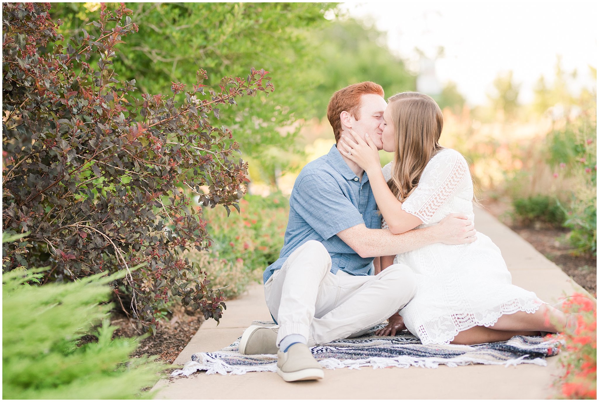 Couple wearing a white lace dress and light blue shirt during candid engagement photos in a Utah garden with flowers and a pond | Kaysville Botanical Garden Engagement | Utah Engagement | Jessie and Dallin Photography