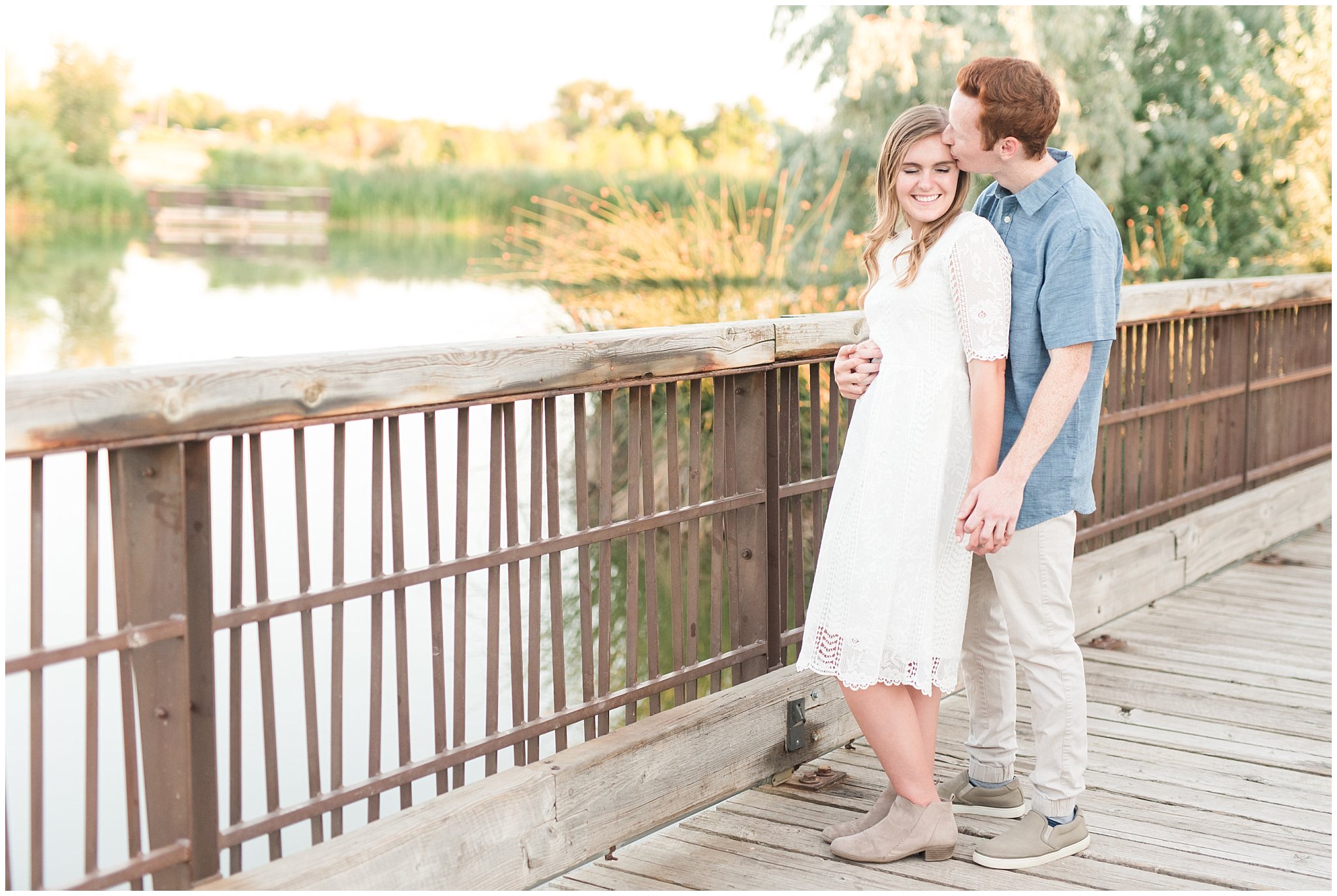 Couple wearing a white lace dress and light blue shirt during candid engagement photos in at a pond with a dock | Kaysville Botanical Garden Engagement | Utah Engagement | Jessie and Dallin Photography