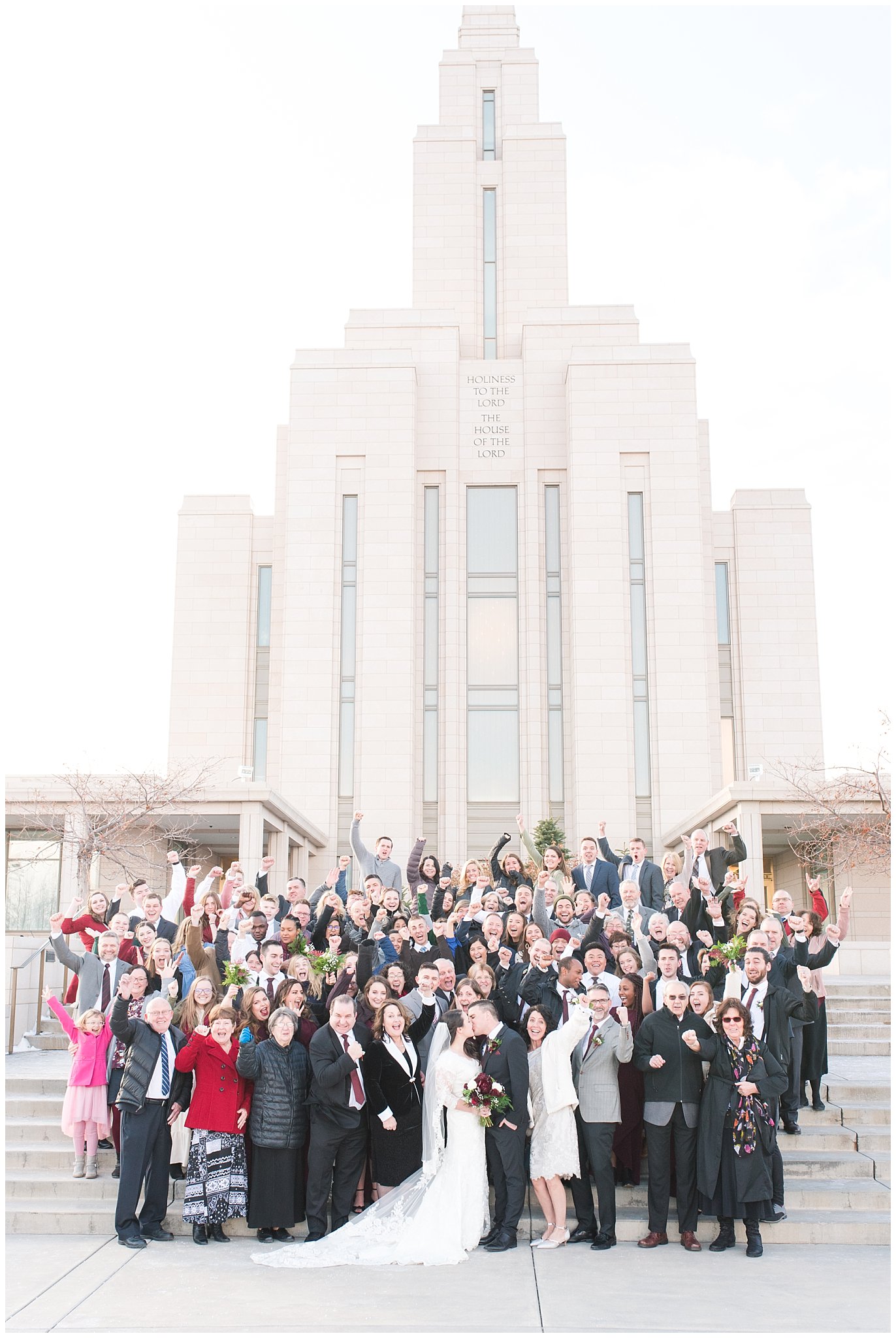 Bride and Groom kiss with family behind them Oquirrh Mountain Temple | Oquirrh Mountain Temple and Gardner Village Wedding | The Gathering Place | Jessie and Dallin Photography