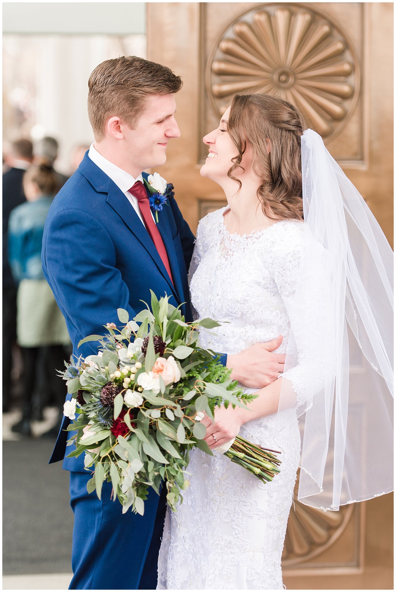 Bride and groom exit the temple with blue suit and burgundy, white and succulent bouquet during winter wedding | Bountiful Temple Wedding and Joseph Smith Memorial Reception | Jessie and Dallin Photography