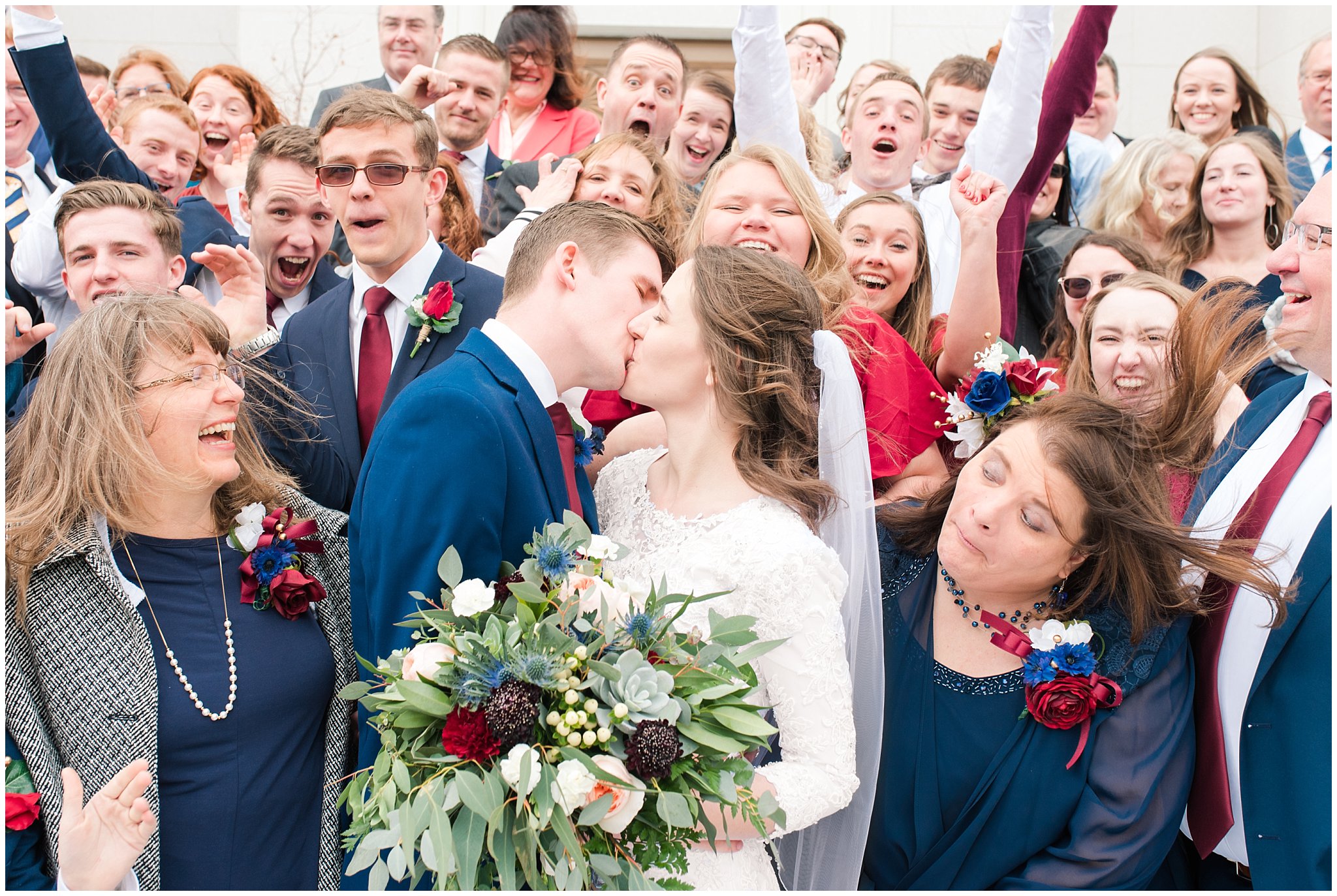 Bride and groom kiss with cheers at the temple with blue suit and burgundy, white and succulent bouquet during winter wedding | Bountiful Temple Wedding and Joseph Smith Memorial Reception | Jessie and Dallin Photography