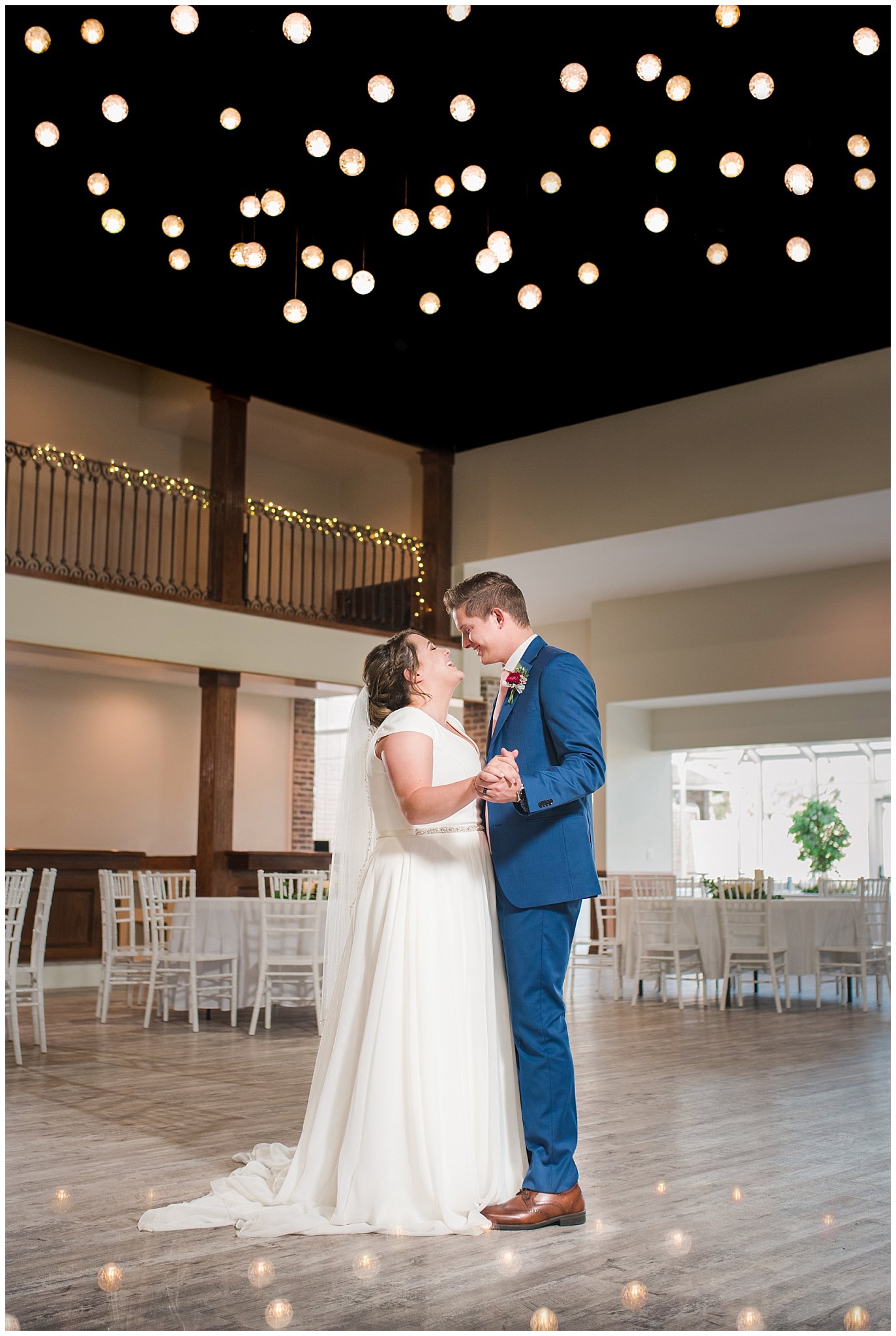 Bride and groom dance until large chandelier in flowy dress and cornish blue suit | Talia Event Center Summer Wedding | Jessie and Dallin Photography