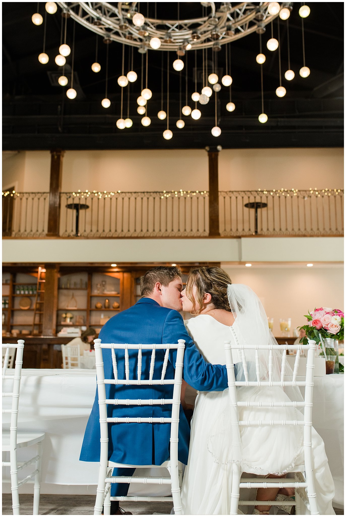 Bride and groom kiss at dinner until chandelier | Talia Event Center Summer Wedding | Jessie and Dallin Photography