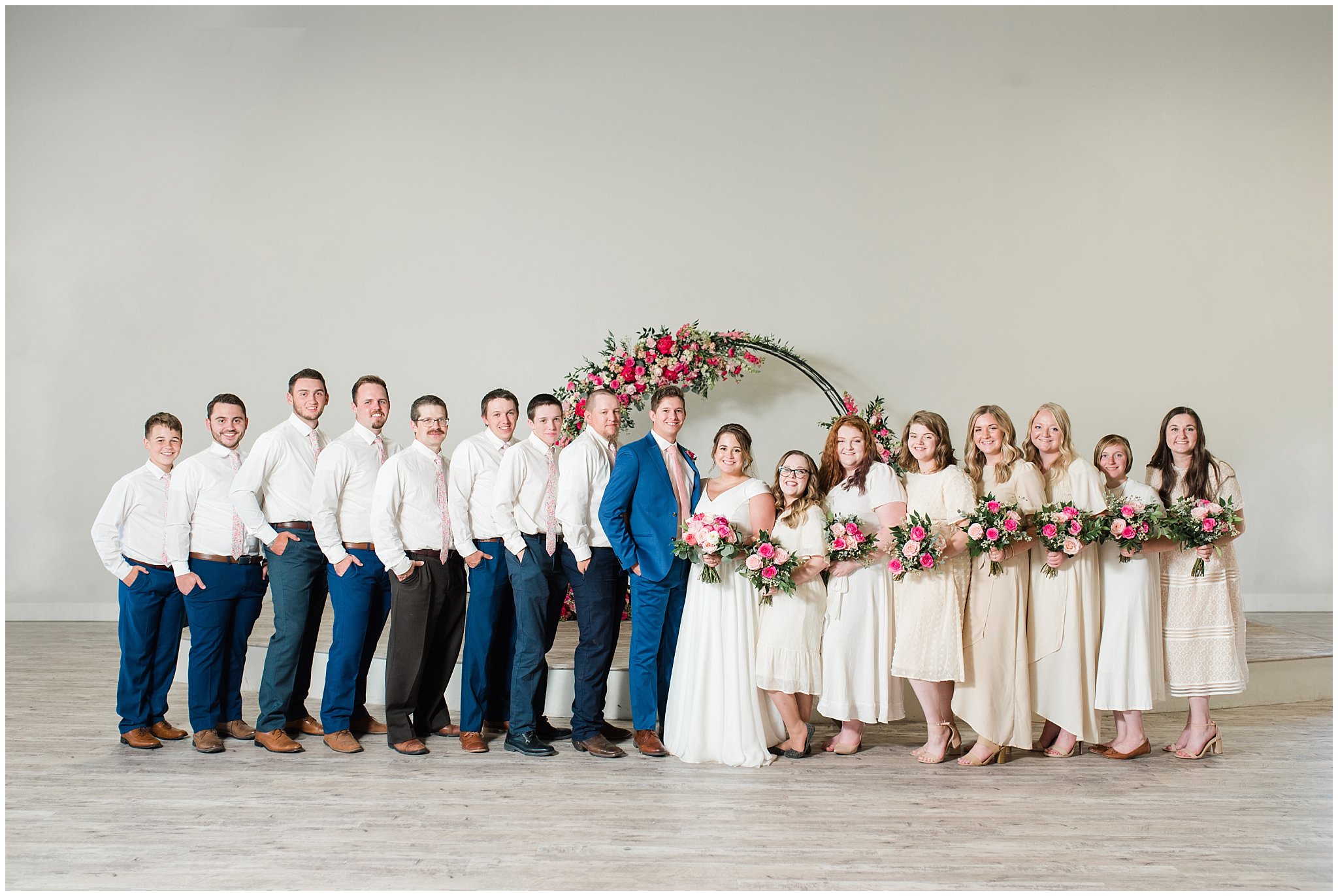 Wedding party wearing floral ties and cream colored dresses in front of floral arch in shades of pink | Talia Event Center Summer Wedding | Jessie and Dallin Photography