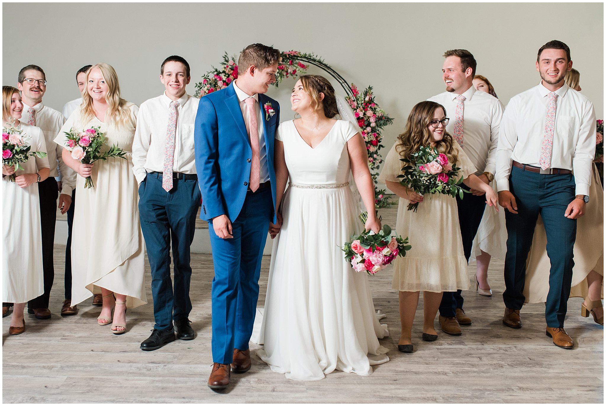 Wedding party wearing floral ties and cream colored dresses in front of floral arch in shades of pink | Talia Event Center Summer Wedding | Jessie and Dallin Photography