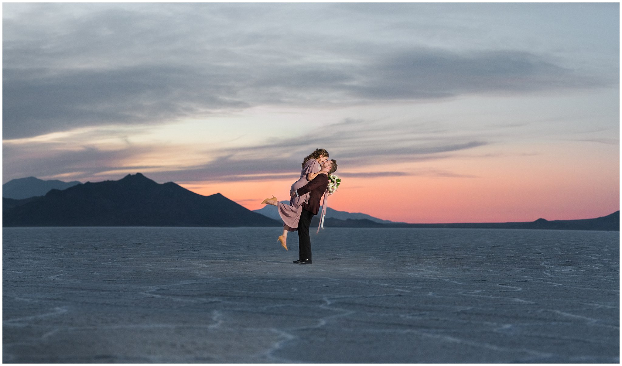 Couple during sunset wearing a dusty rose dress and burgundy suit with white and pink bouquet at the Bonneville Salt Flats | Bonneville Salt Flats Milky Way Anniversary Session | Jessie and Dallin Photography