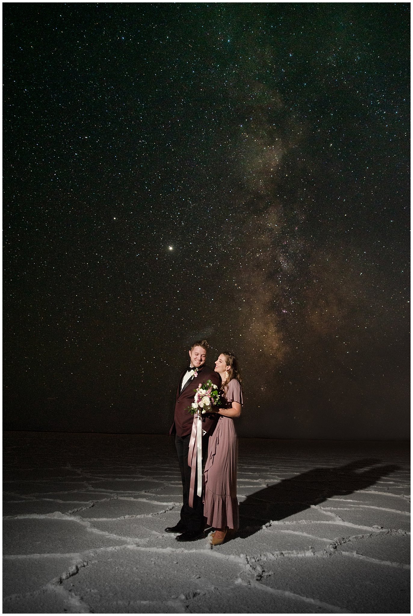 Astrophotography with couple wearing a dusty rose dress and burgundy suit with white and pink bouquet at the Bonneville Salt Flats Milky Way Anniversary Session | Jessie and Dallin Photography