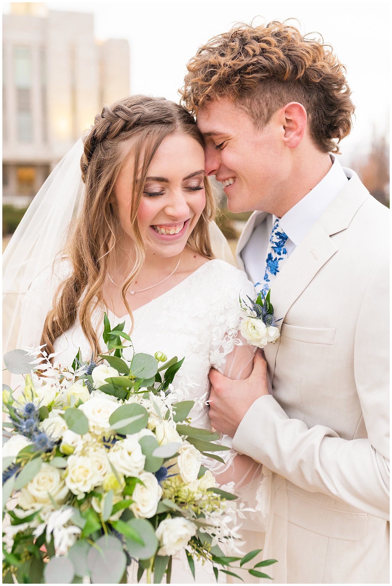 Bride and groom portraits at the temple. Groom in cream colored suit with blue floral tie and bride with lace dress and white floral bouquet. | Oquirrh Mountain Temple and Draper Day Barn Winter Wedding | Jessie and Dallin Photography