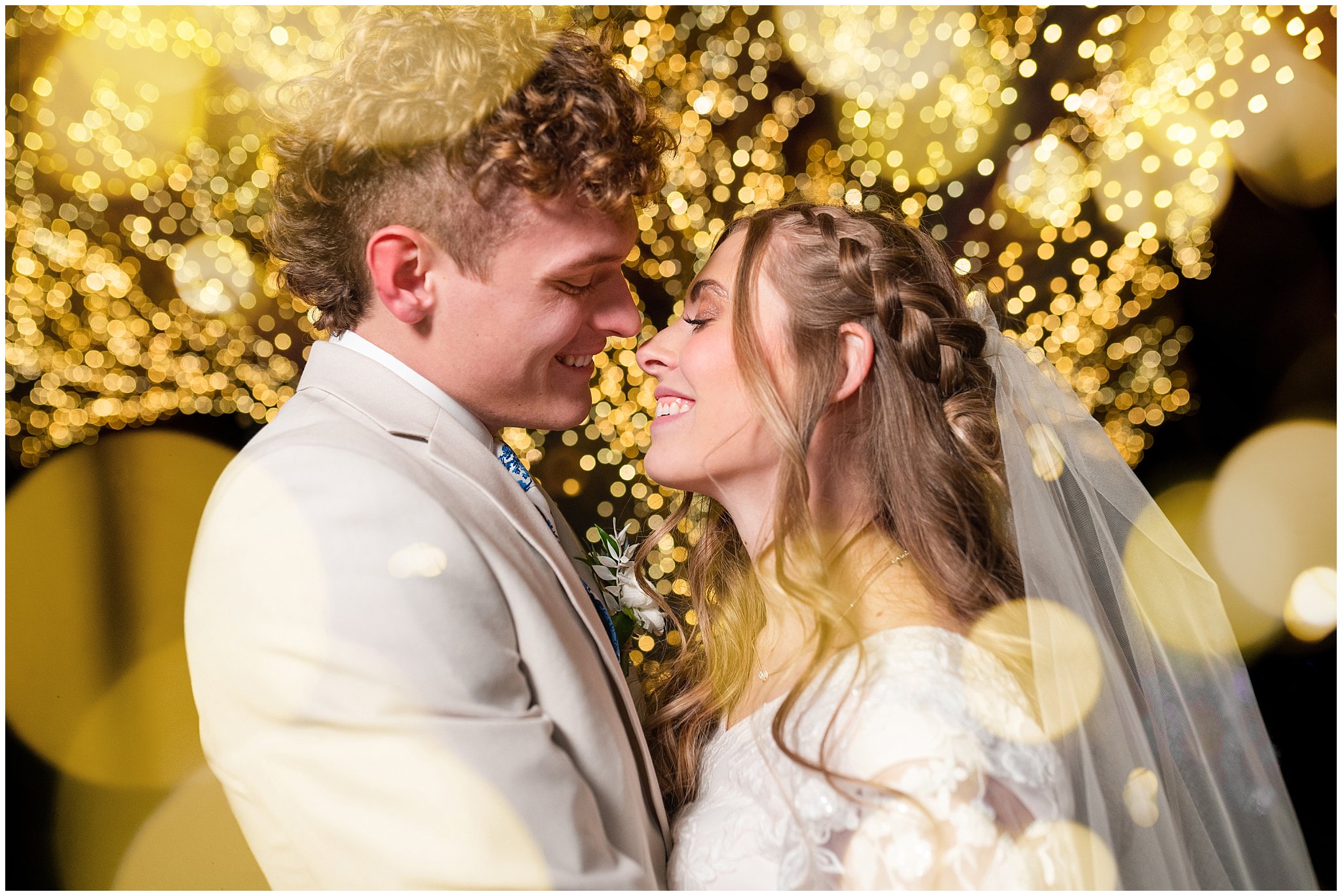 Bride and groom portraits with Christmas lights at the Tree of Life at Draper Park. Groom in cream colored suit with blue floral tie and bride with lace dress and white floral bouquet. | Oquirrh Mountain Temple and Draper Day Barn Winter Wedding | Jessie and Dallin Photography