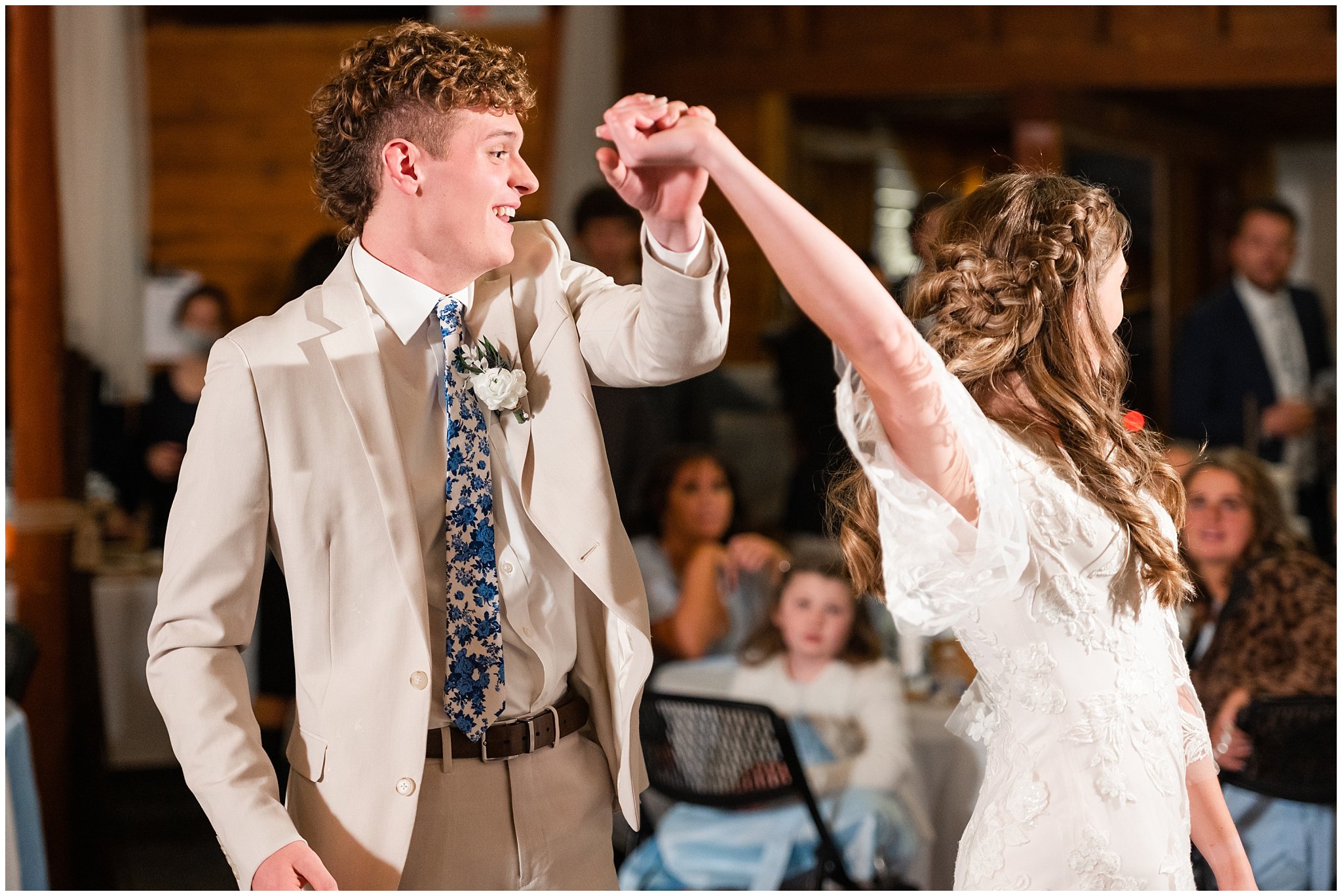 Bride and groom share first dance at their reception. Groom in cream colored suit with blue floral tie and bride in lace detailed wedding dress | Oquirrh Mountain Temple and Draper Day Barn Winter Wedding | Jessie and Dallin Photography