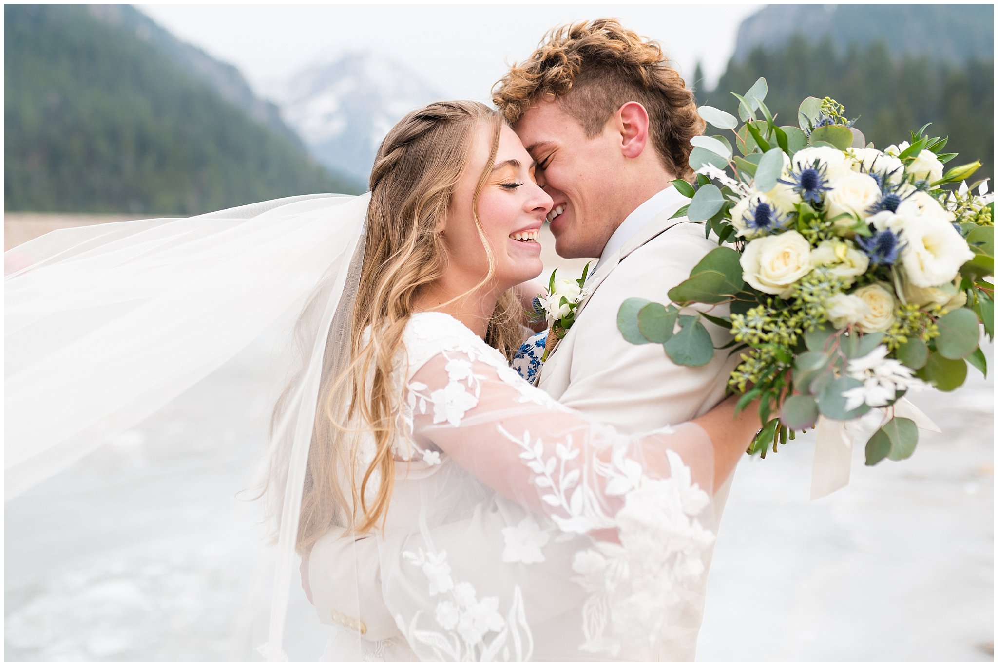 Bride in the mountains on frozen lake wearing lace dress with veil and white floral bouquet | Tibble Fork Winter Formal Session | Jessie and Dallin Photography