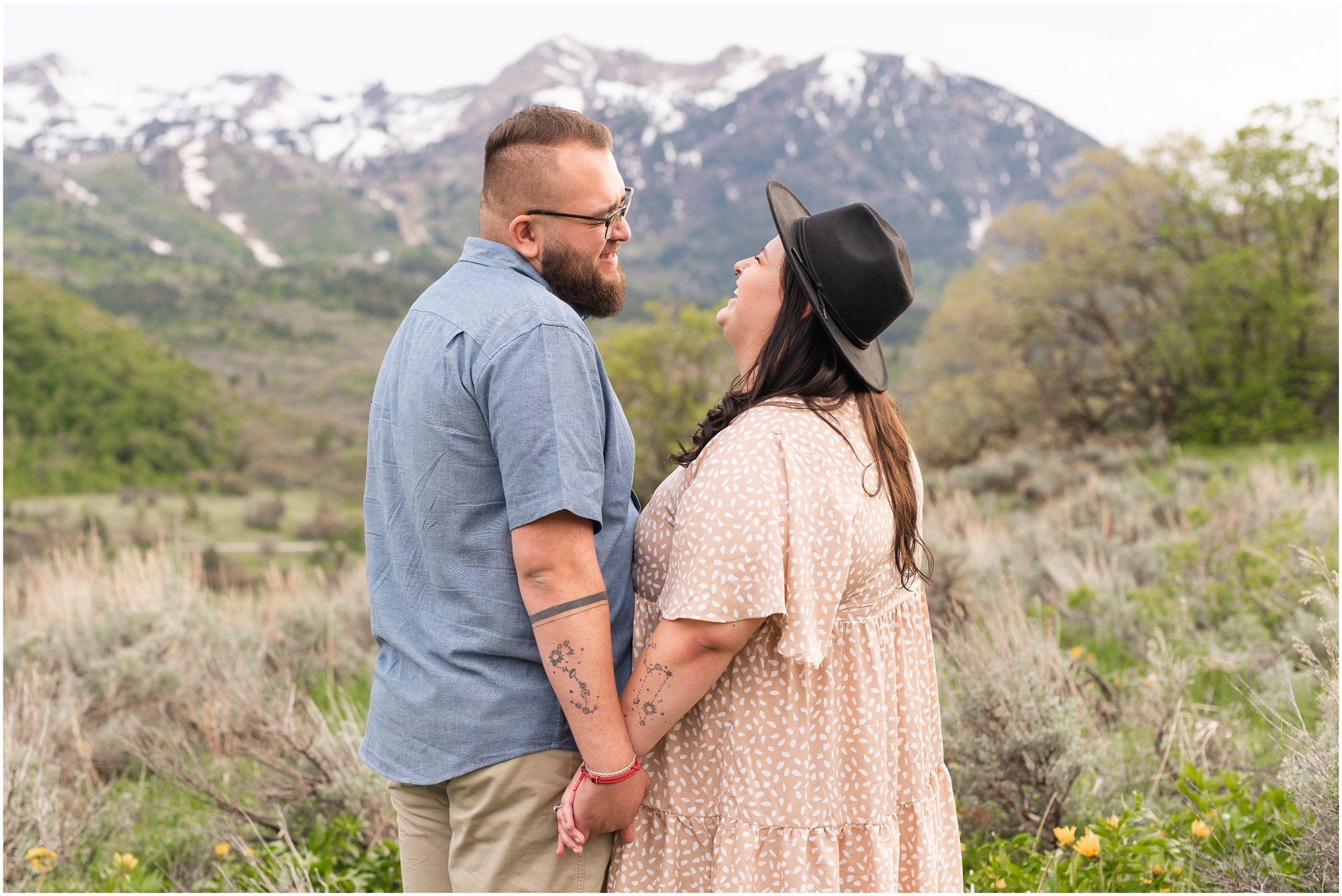 Couple during engagement session in yellow sunflower wildflowers surrounded by snowy mountain peaks | Ogden Valley Summer Engagement Session
