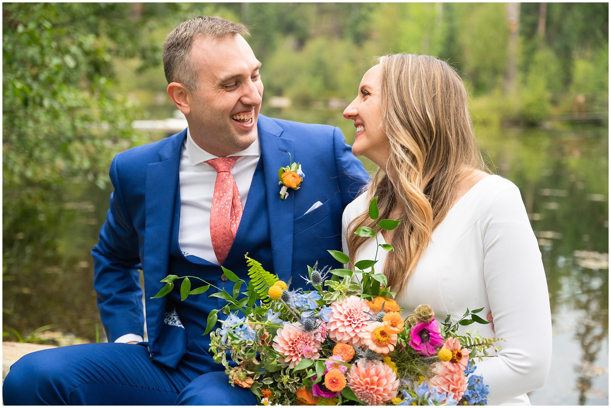 Bride and groom portraits with an elegant fitted dress and blue suit with coral tie, and wildflower bouquet in the Montana forest and near a pond | Mountainside Weddings Kalispell Montana Destination Wedding | Jessie and Dallin Photography