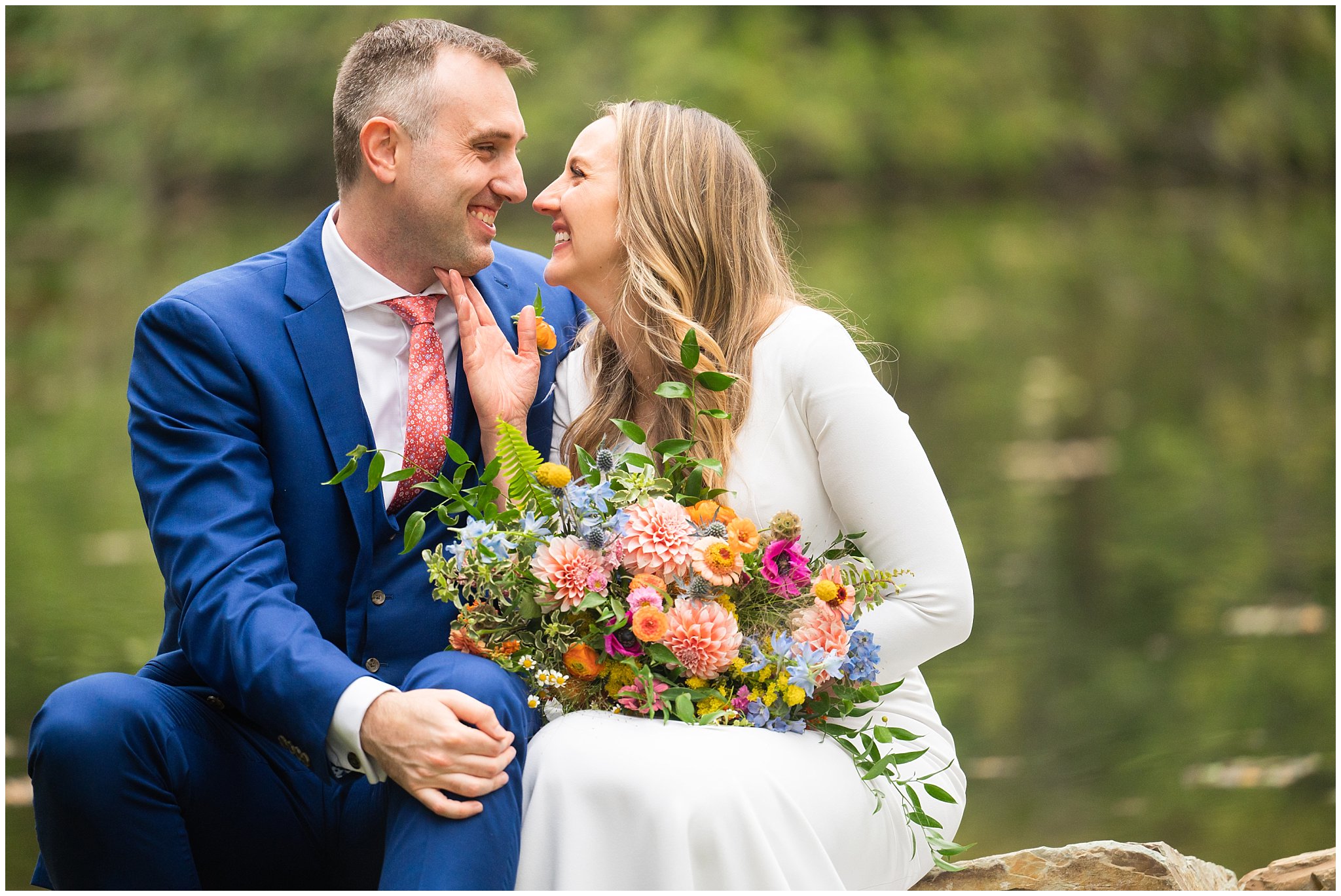 Bride and groom portraits with an elegant fitted dress and blue suit with coral tie, and wildflower bouquet in the Montana forest and near a pond | Mountainside Weddings Kalispell Montana Destination Wedding | Jessie and Dallin Photography