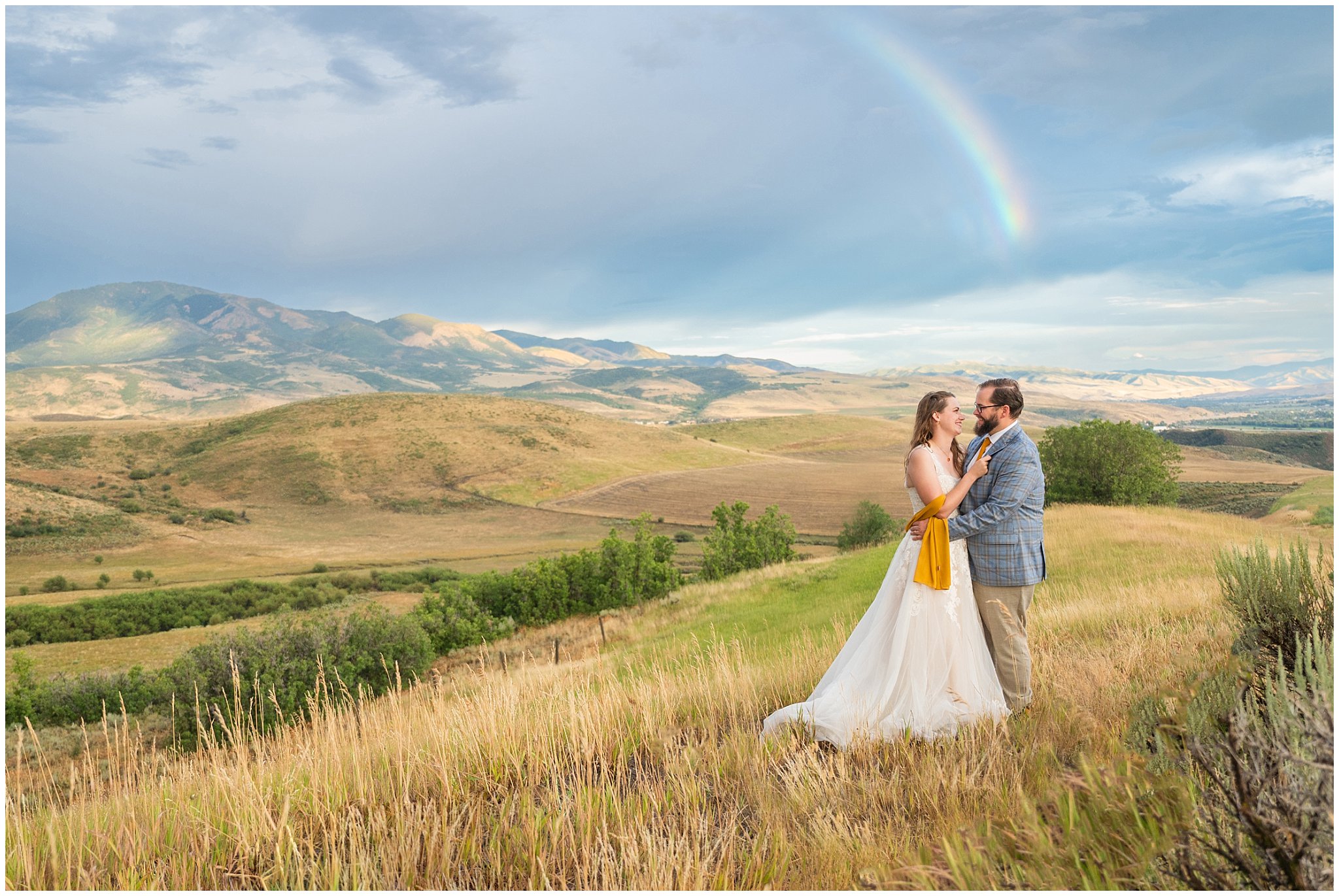 Bride and groom in flowy wedding dress and blue and gold plaid suit in the mountains surrounded by sunset skies, rainbows, and Aspen trees | Rainy Snowbasin Wedding Formal Session | Jessie and Dallin Photography