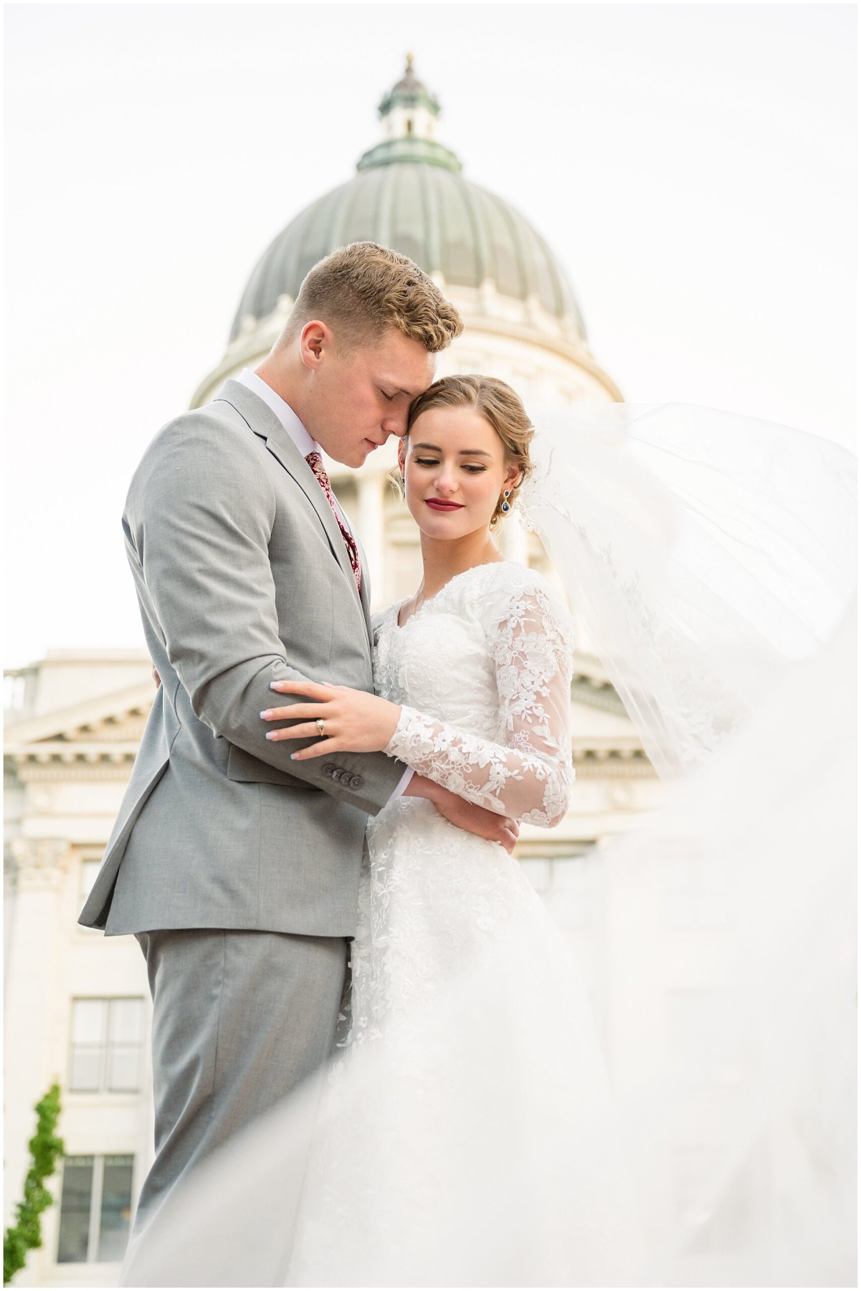 Bride and groom share a romantic moment while wearing a long cathedral length veil with the Utah State Capitol behind them | Sunset Utah State Capitol Wedding Formal Session | Jessie and Dallin Photography