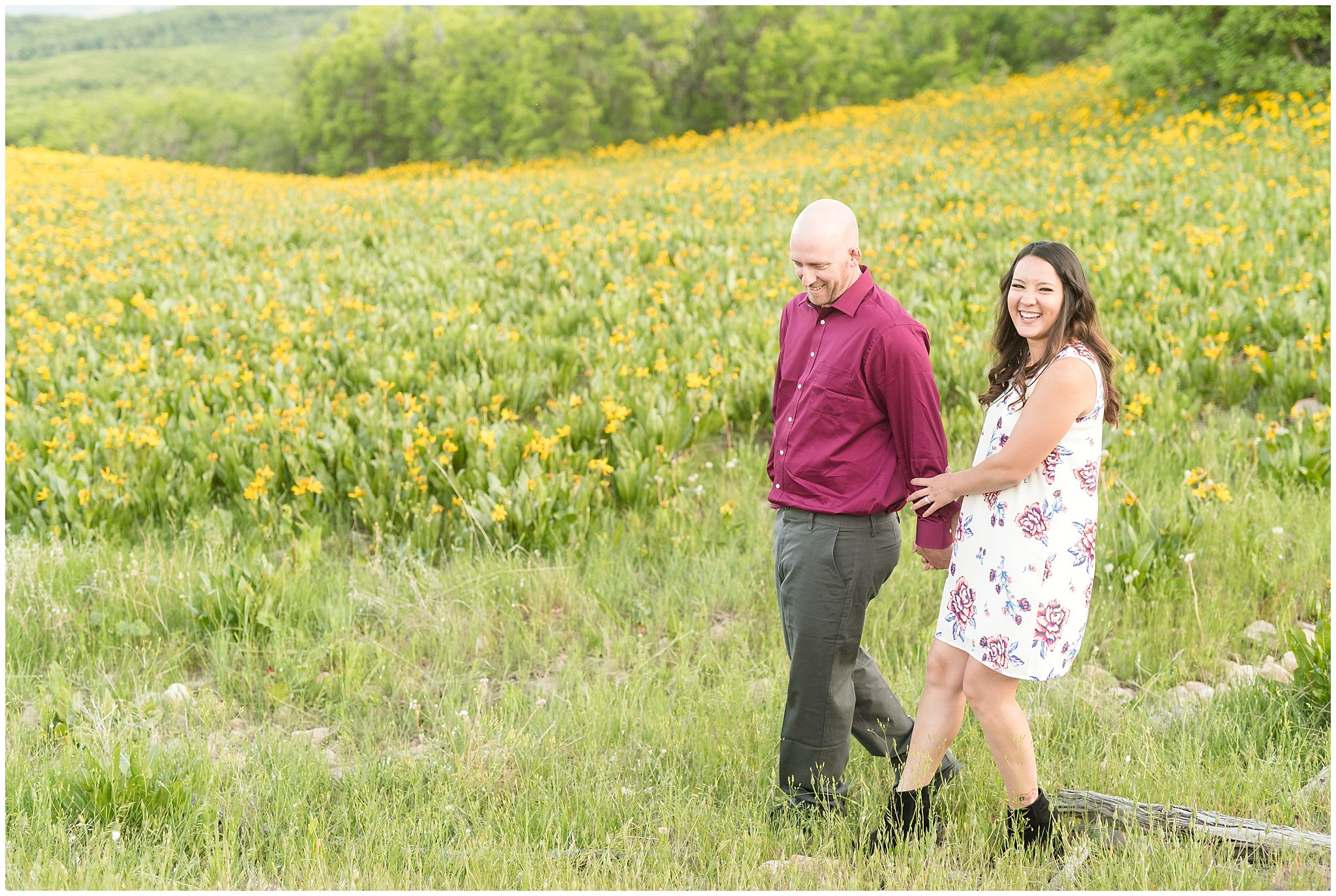 Couple walking during engagement session with mountains in the background and wildflowers | Snowbasin Utah Engagements