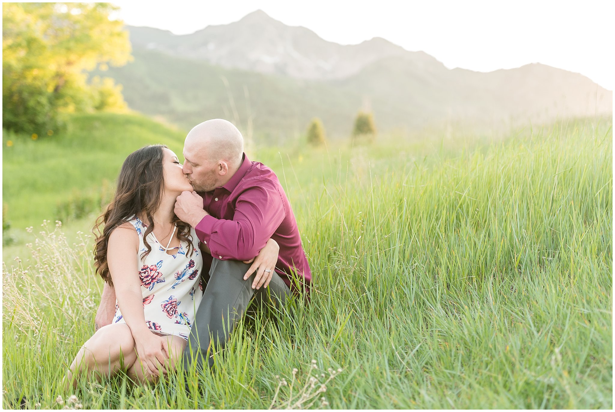 Couple kissing during engagement session with mountains in the background and wildflowers | Snowbasin Utah Engagements