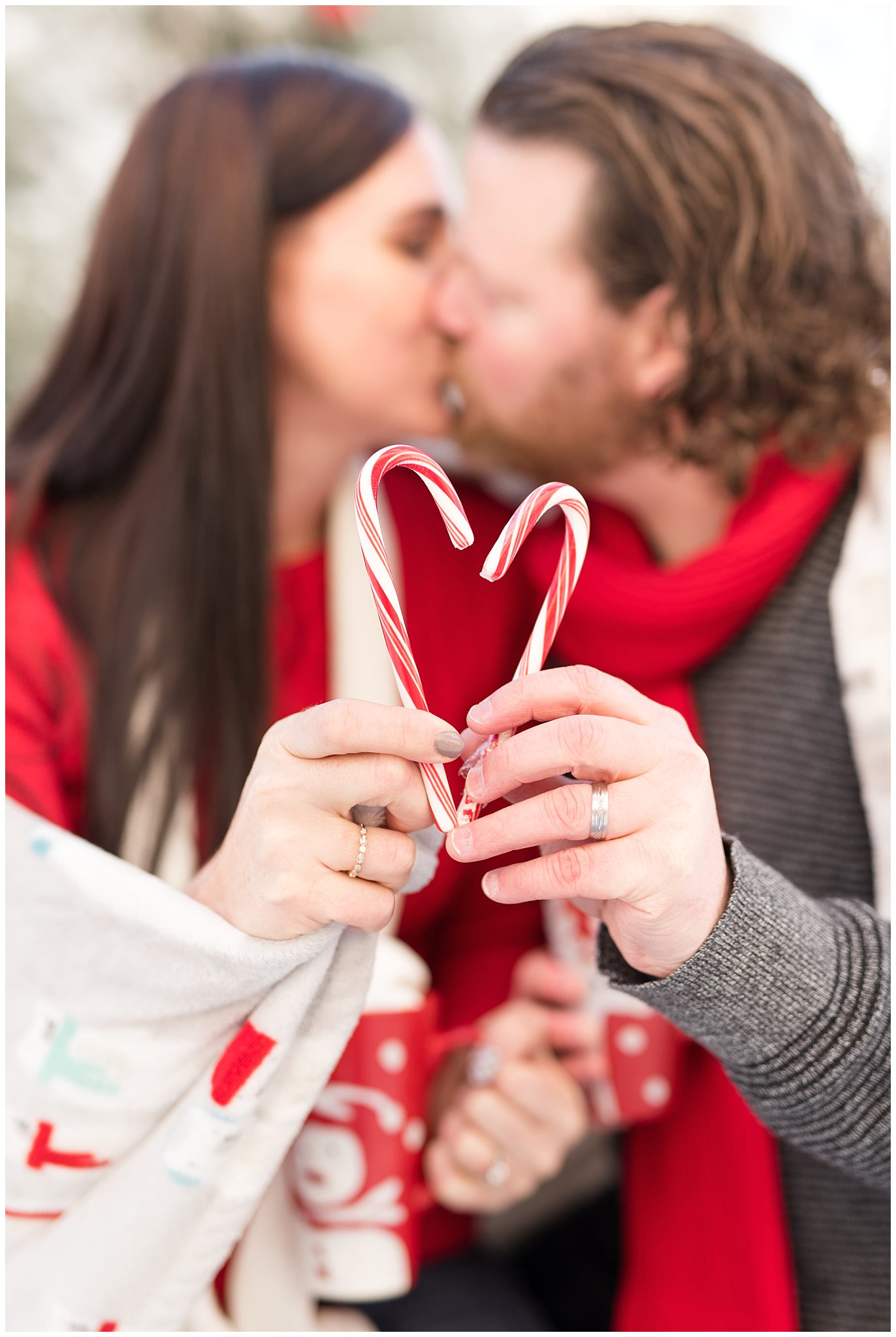 Couple holding up candy cane heart and kissing in the snow | Utah Family Christmas Photoshoot | Oak Hills Reception and Event | Jessie and Dallin Photography