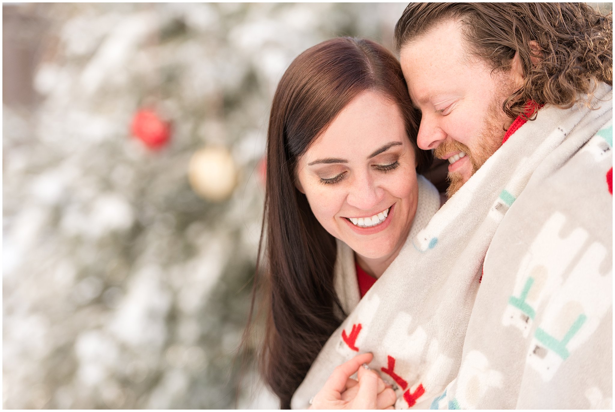 Couple cuddled up close in Christmas blanket in front of Christmas trees | Utah Family Christmas Photoshoot | Oak Hills Reception and Event | Jessie and Dallin Photography