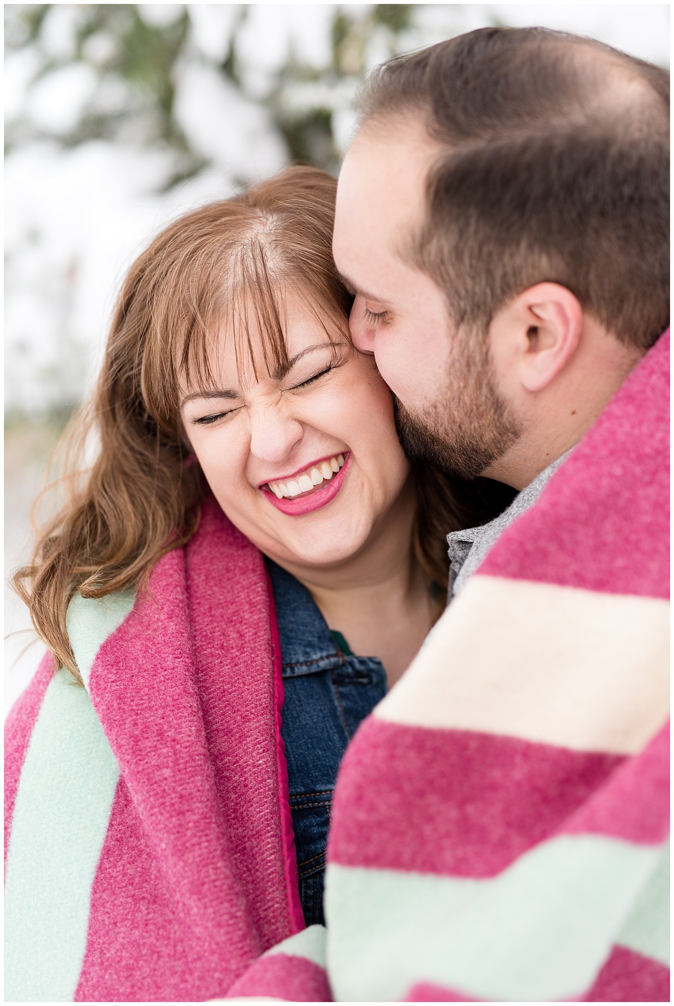 Couple wrapped in blanket in the winter and guy gives girl a kiss on the cheek |  Winter Engagement at Mueller Park and the Utah State Capitol | Jessie and Dallin Photography