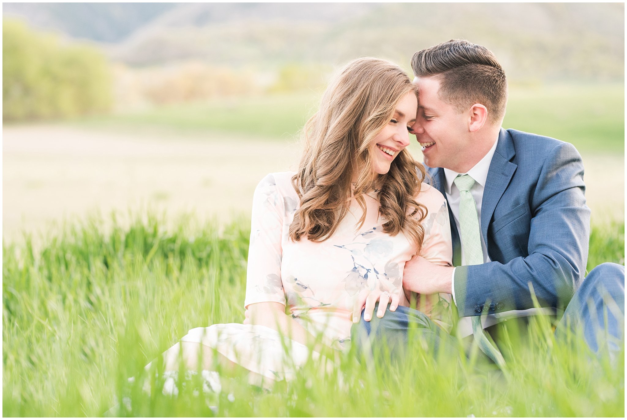 Couple dressed in blue suit and blush dress surrounded by grass and snowy mountain peaks | Downtown Logan and Wellsville Mountain Engagement | Jessie and Dallin Photography