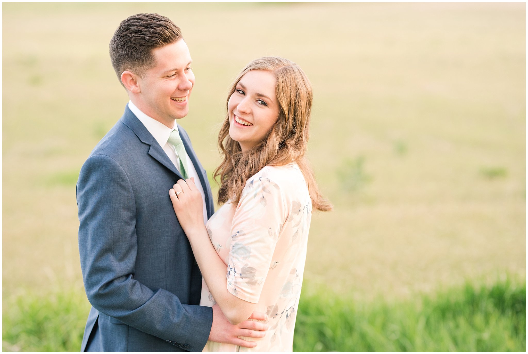 Couple dressed up in blue suit and blush dress surrounded by grass and snowy mountain peaks during elegant engagement | Downtown Logan and Wellsville Mountain Engagement | Jessie and Dallin Photography