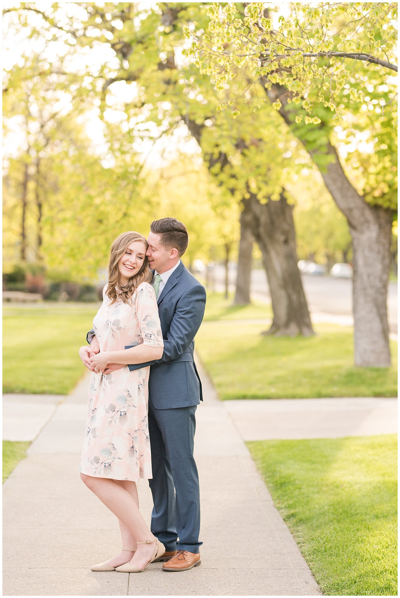 Couple dressed up in blue suit and blush dress surrounded by the city and trees in the spring | Downtown Logan and Wellsville Mountain Engagement | Jessie and Dallin Photography