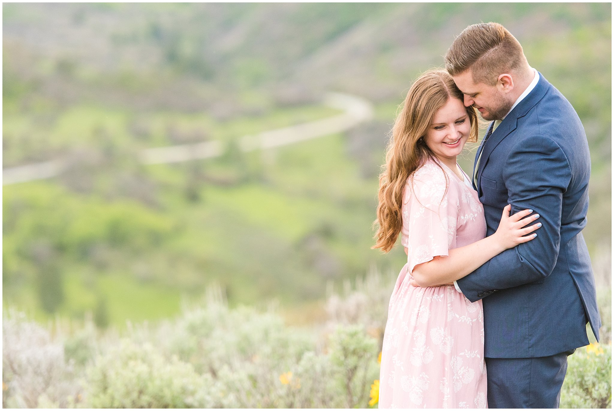 Couple dressed in blush dress and blue suit surrounded by sunflowers and snowy mountains | Ogden Valley Spring Mountain Engagement | Jessie and Dallin Photography