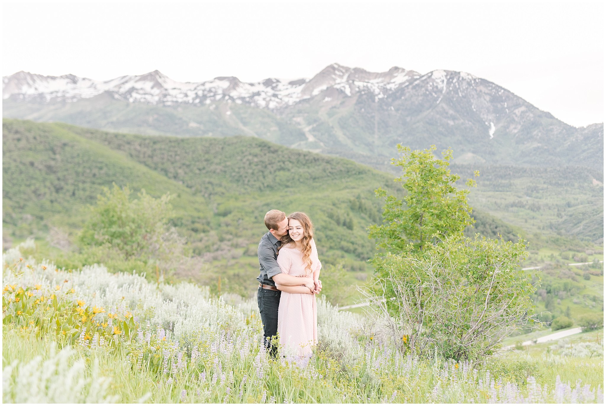 Couple in blush dress and grey and black buttoned shirt in front of a mountain view | Trapper's Loop Mountain Engagement | Utah Mountain Engagement Session | Jessie and Dallin Photography