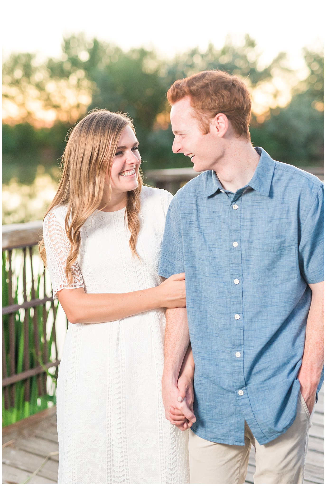 Couple wearing a white lace dress and light blue shirt during candid engagement photos in at a pond with a dock | Kaysville Botanical Garden Engagement | Utah Engagement | Jessie and Dallin Photography