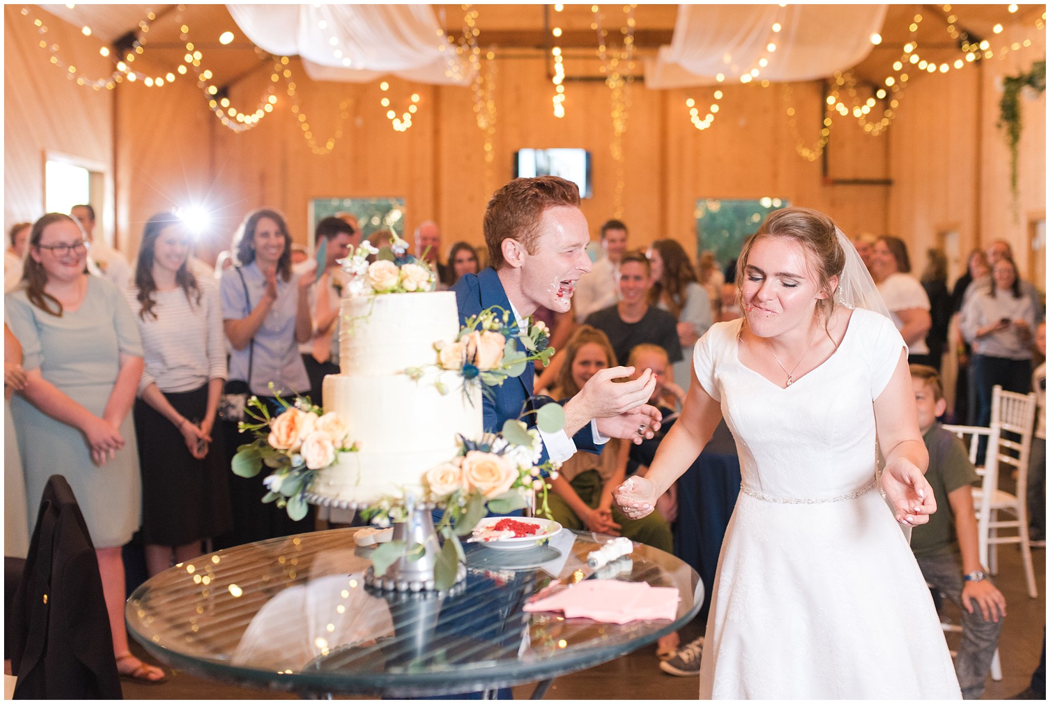 Bride and groom with a cake smash | white three tier cake with roses and blue thistles | Oak Hills Reception and Events Center | Jessie and Dallin Photography