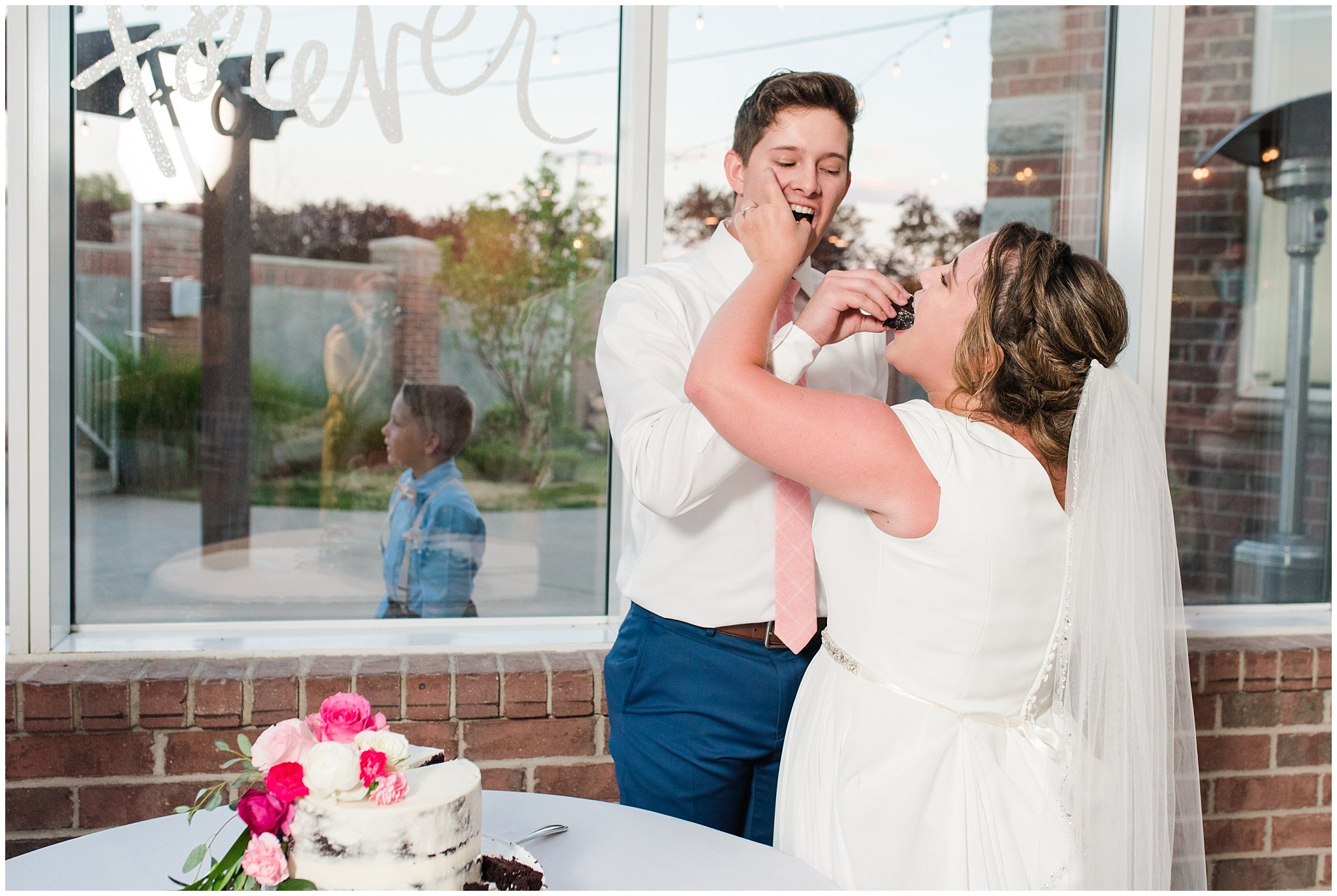 Bride and groom cut cookies and cream cake in front of windows and covered with pink and white florals | Talia Event Center Summer Wedding | Jessie and Dallin Photography