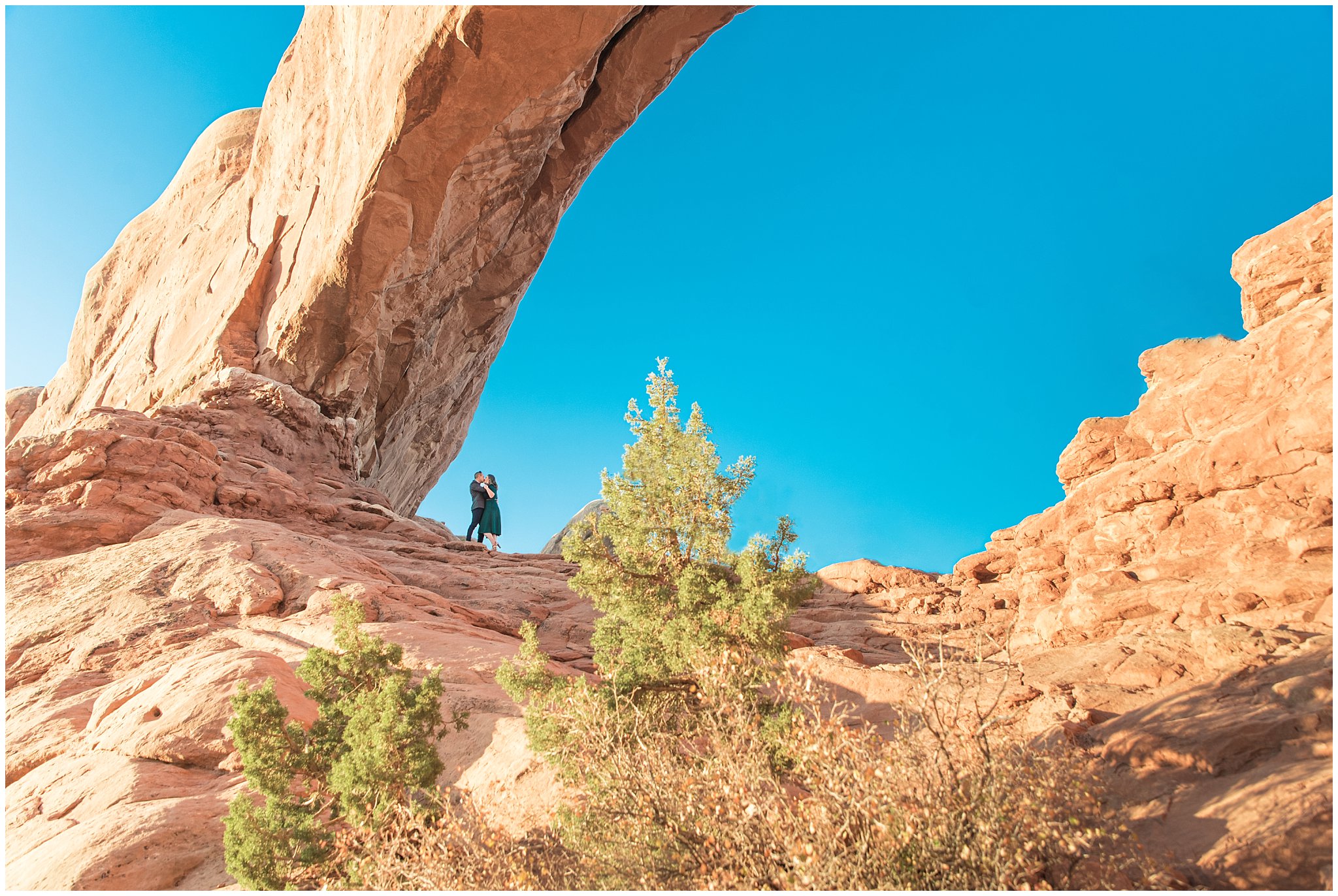 Couple dressed in green dress and grey and blue suit with bowtie for adventure engagement session at Arches National Park and Dead Horse Point Engagement | Jessie and Dallin Photography