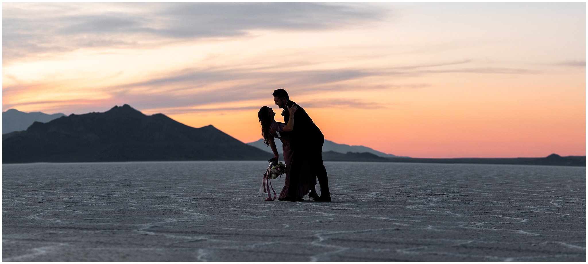 Couple during sunset wearing a dusty rose dress and burgundy suit with white and pink bouquet at the Bonneville Salt Flats | Bonneville Salt Flats Milky Way Anniversary Session | Jessie and Dallin Photography