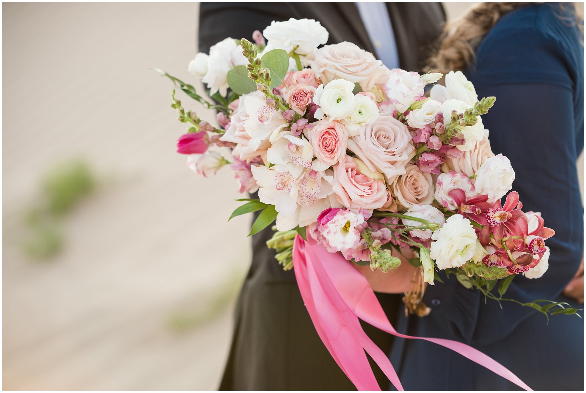 Couple dressed in black suit and blue flowy dress with white and pink orchid floral bouquet during couples session | Little Sahara Sand Dunes Milky Way Engagement Session