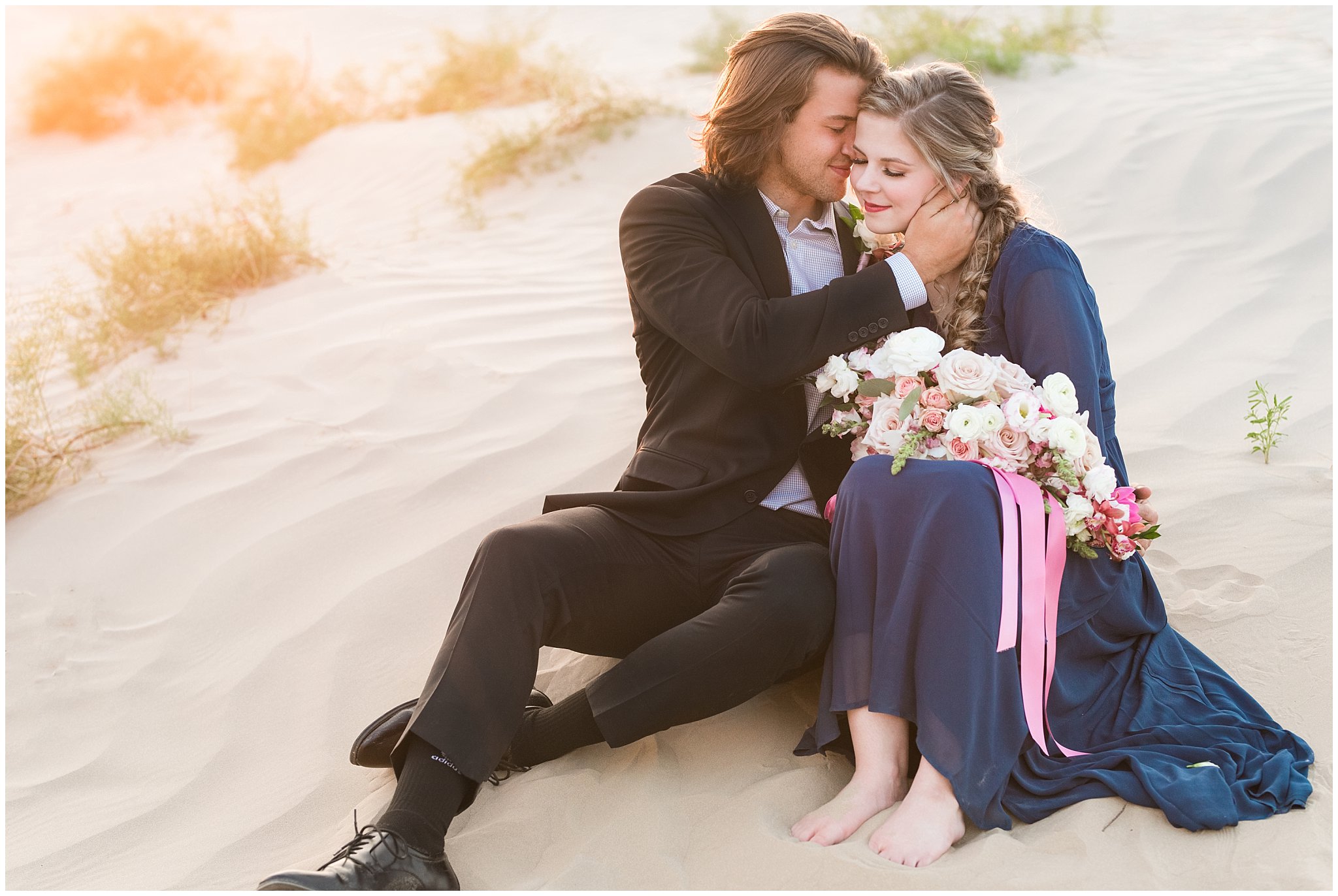 Couple dressed in black suit and blue flowy dress with white and pink orchid floral bouquet during couples session | Little Sahara Sand Dunes Milky Way Engagement Session