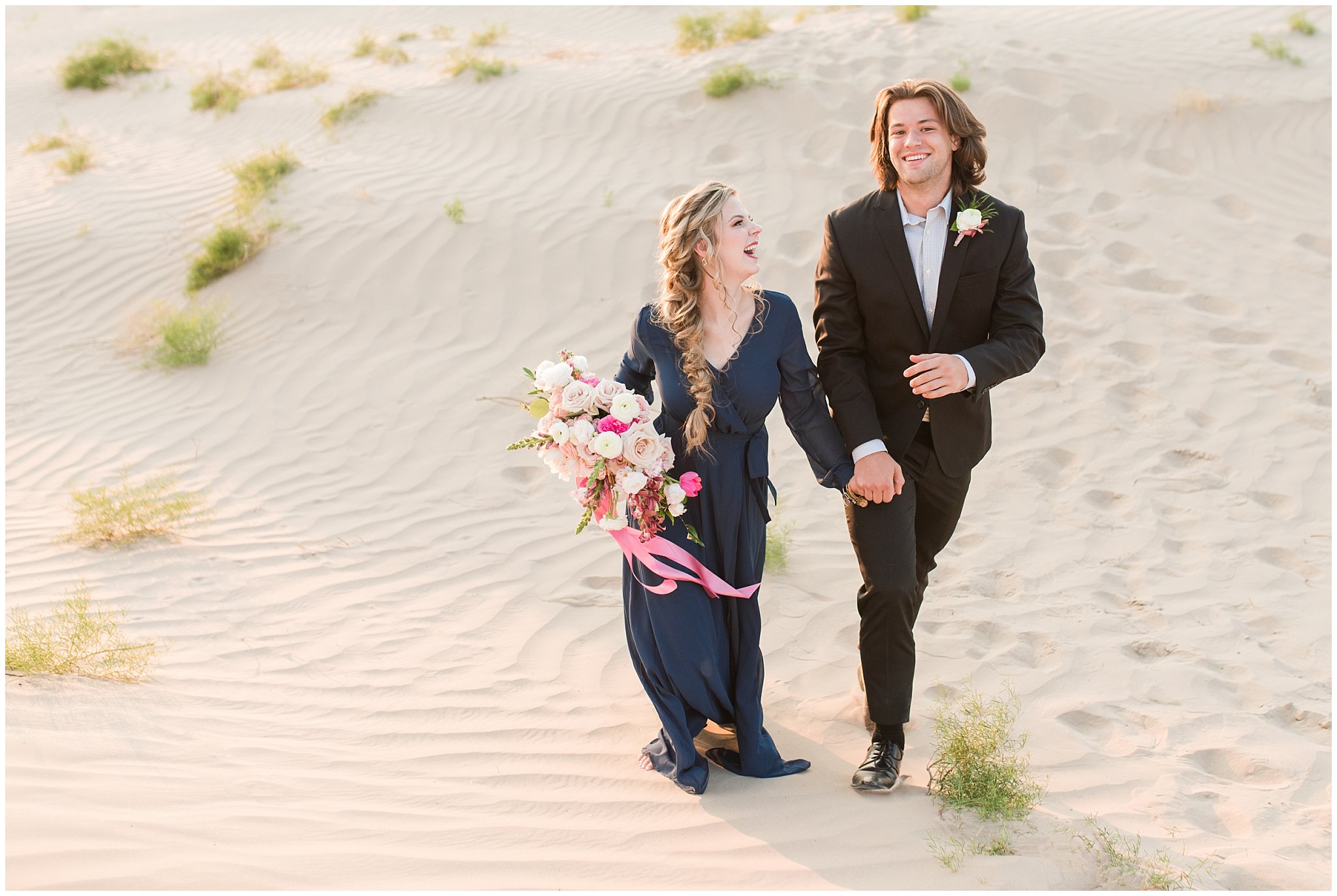 Couple dressed in black suit and blue flowy dress with white and pink orchid floral bouquet during couples session | Little Sahara Sand Dunes Milky Way Engagement Session