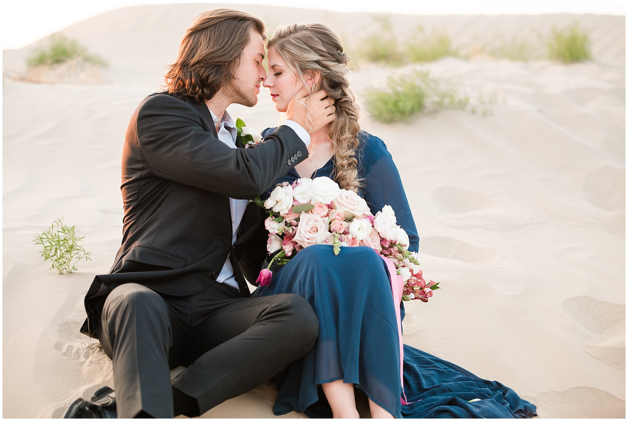 Couple dressed in black suit and blue flowy dress with white and pink orchid floral bouquet during couples session | Little Sahara Sand Dunes Milky Way Engagement Session