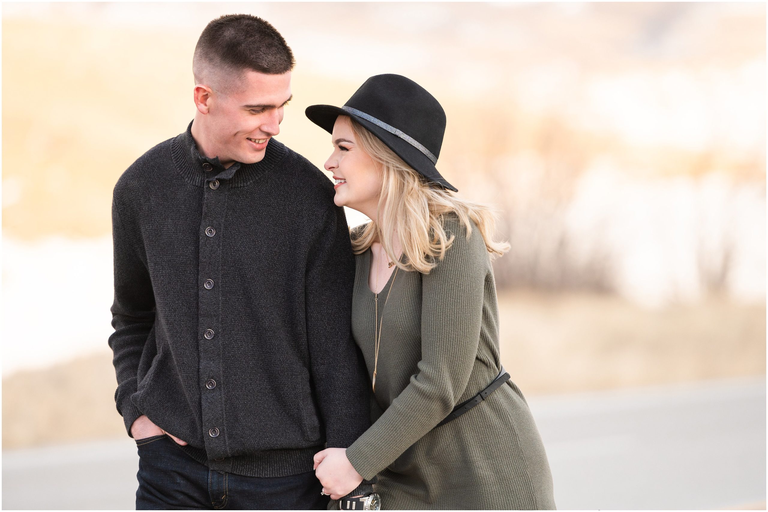 Couple in the snow during mountain destination engagement session in Utah | Wearing olive colored dress with black floppy hat and black sweater and black pants | Snowbasin Resort Snowy Engagement Session | Jessie and Dallin Photography