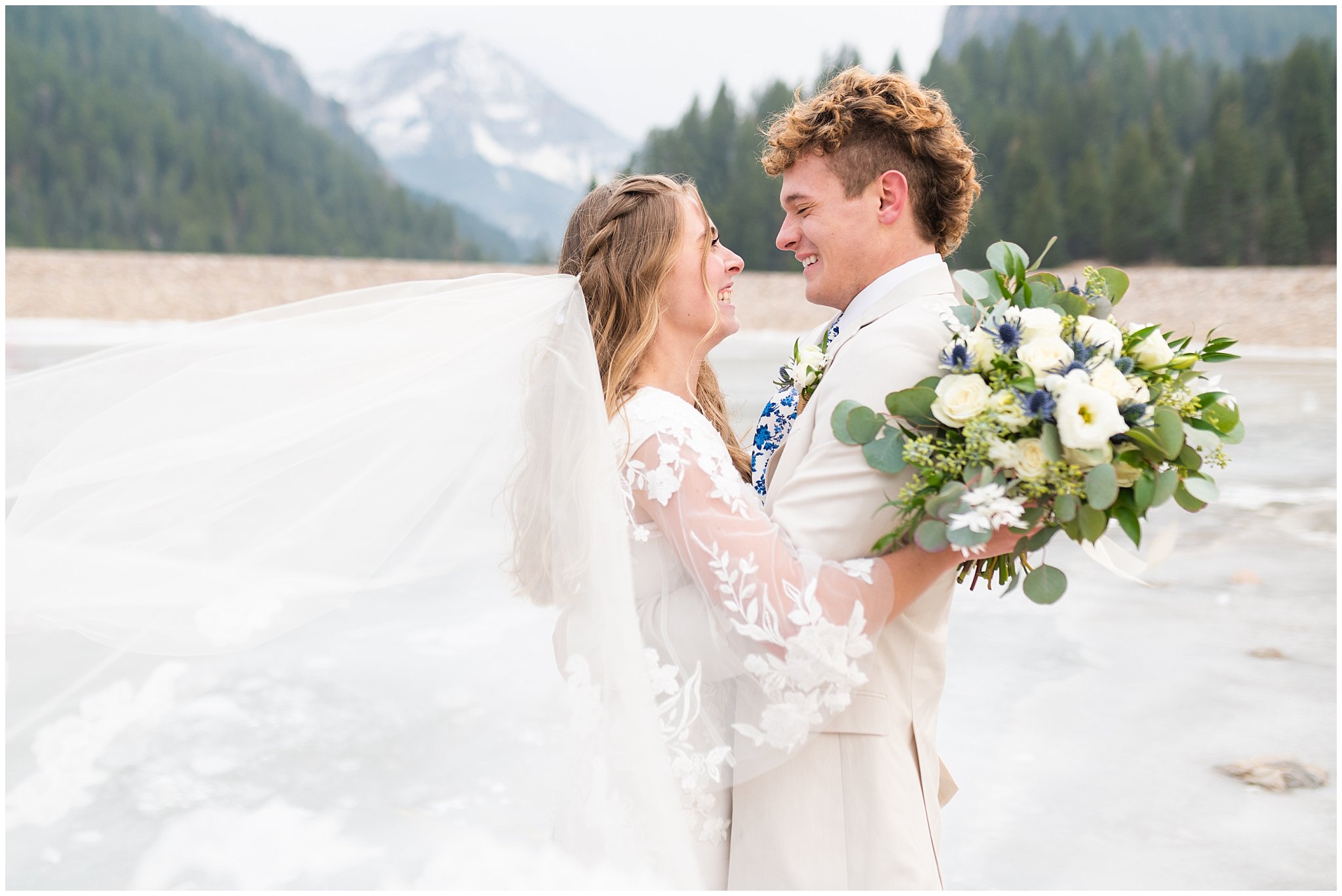 Bride in the mountains on frozen lake wearing lace dress with veil and white floral bouquet | Tibble Fork Winter Formal Session | Jessie and Dallin Photography