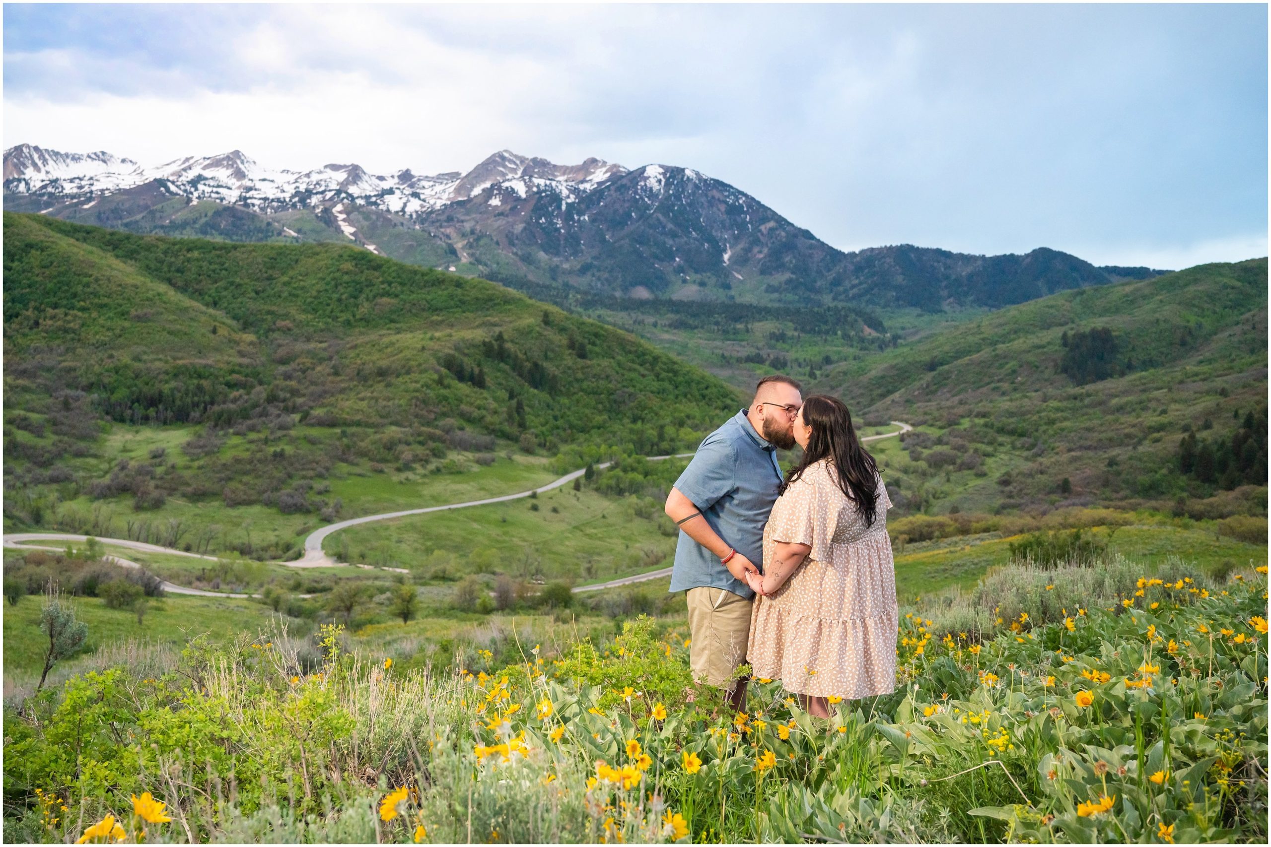 Couple during engagement session in yellow sunflower wildflowers surrounded by snowy mountain peaks | Ogden Valley Summer Engagement Session