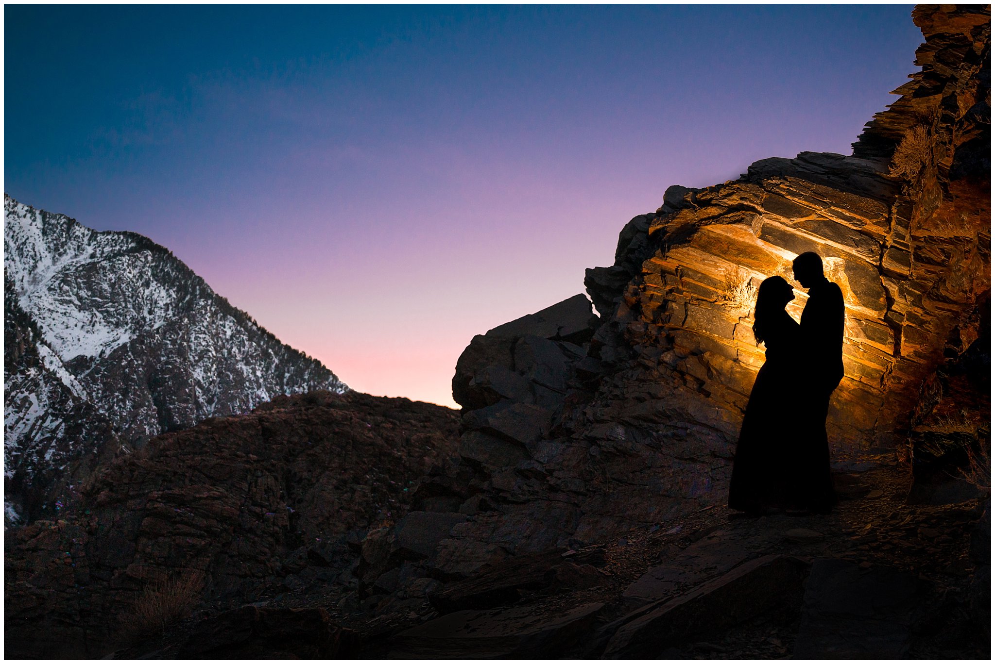 Couple dressed up in formal outfits sharing candid moments in the Utah mountains in the snow and silhouetted against the mountain boulders | Big Cottonwood Canyon Winter Engagement Session | Jessie and Dallin Photography