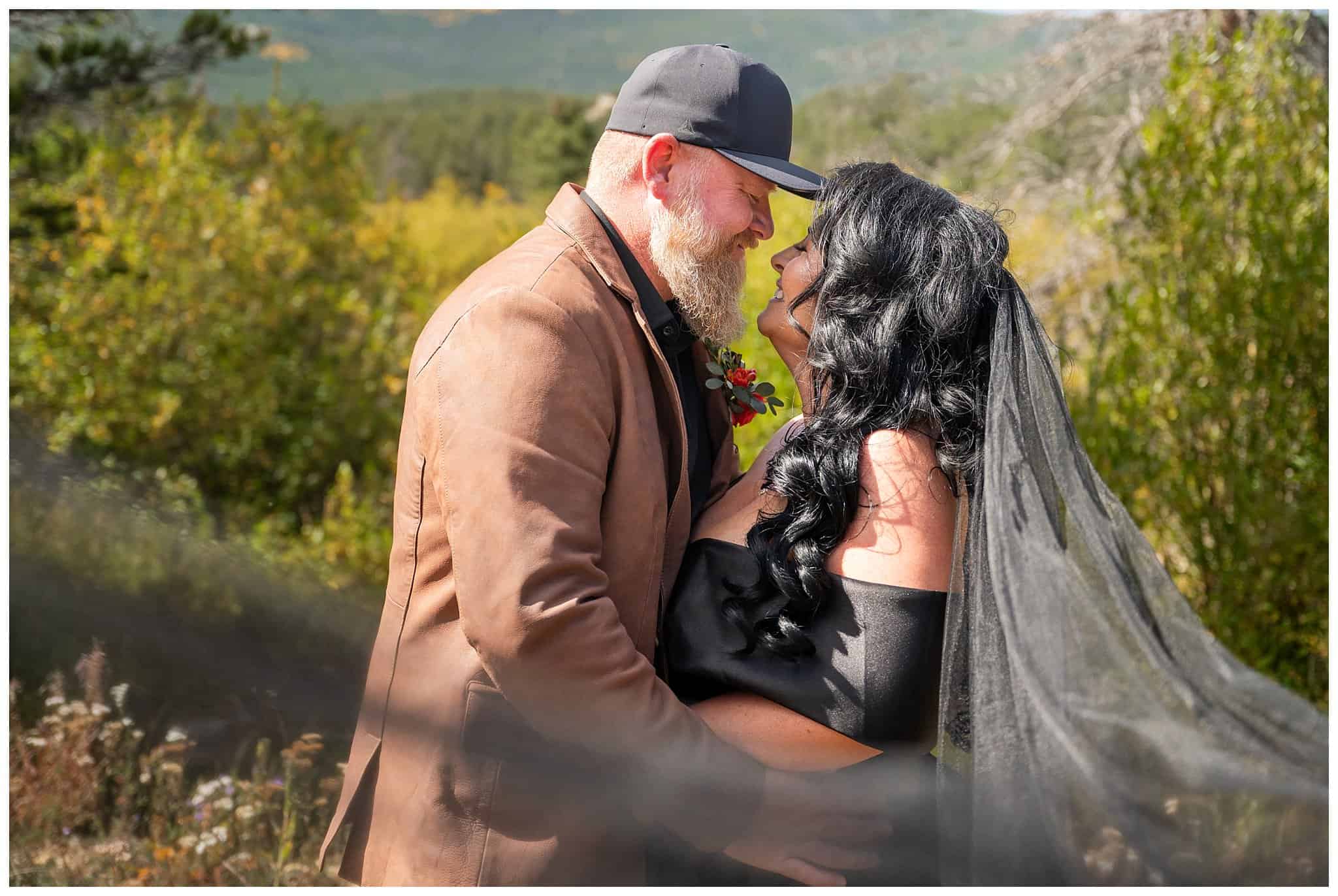 Bride in black wedding dress and veil and groom in leather brown jacket and hat share moments together outside of the Church on the Rock at Estes Park | Fall Rocky Mountain National Park Elopement | Jessie and Dallin Photography